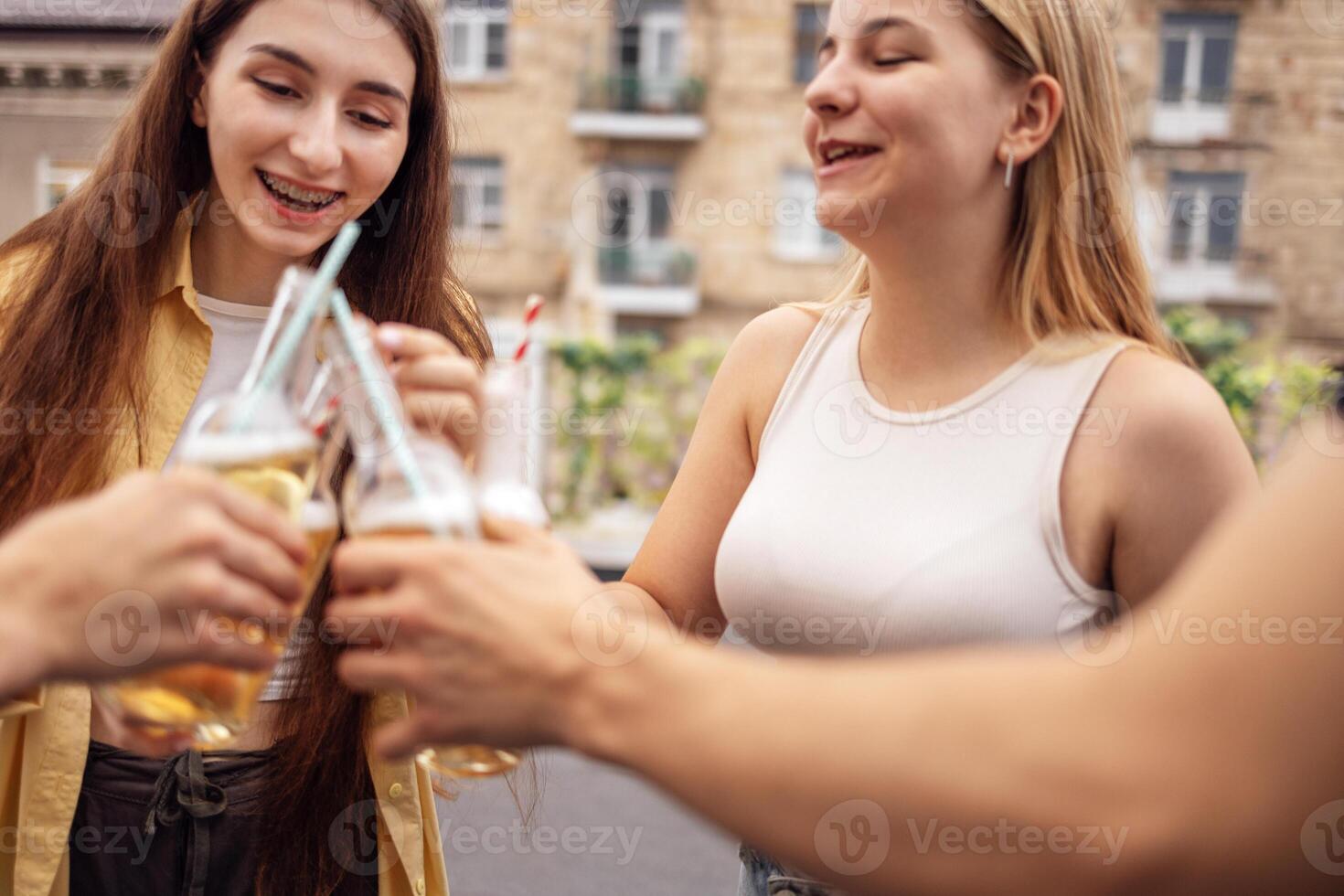 Group of teenagers are having fun and drinking lemonade on street. Cute friends raise toast and clink glasses with delicious cocktails. photo