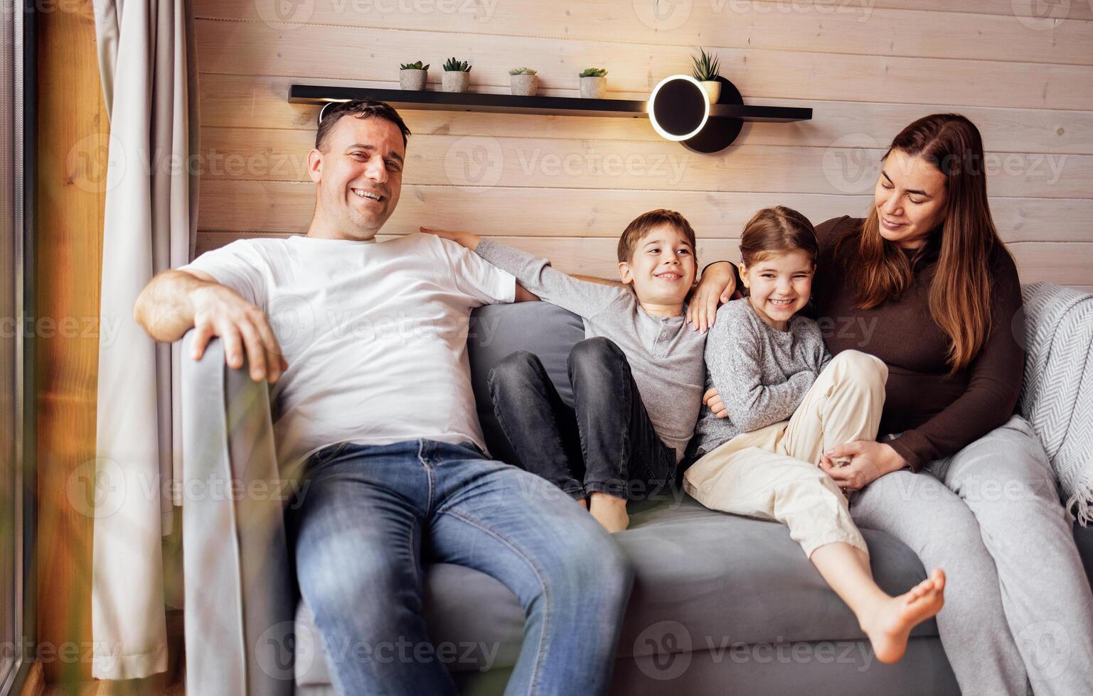 Young happy family is relaxing at home. Little children and their smiling parents are sitting on couch photo