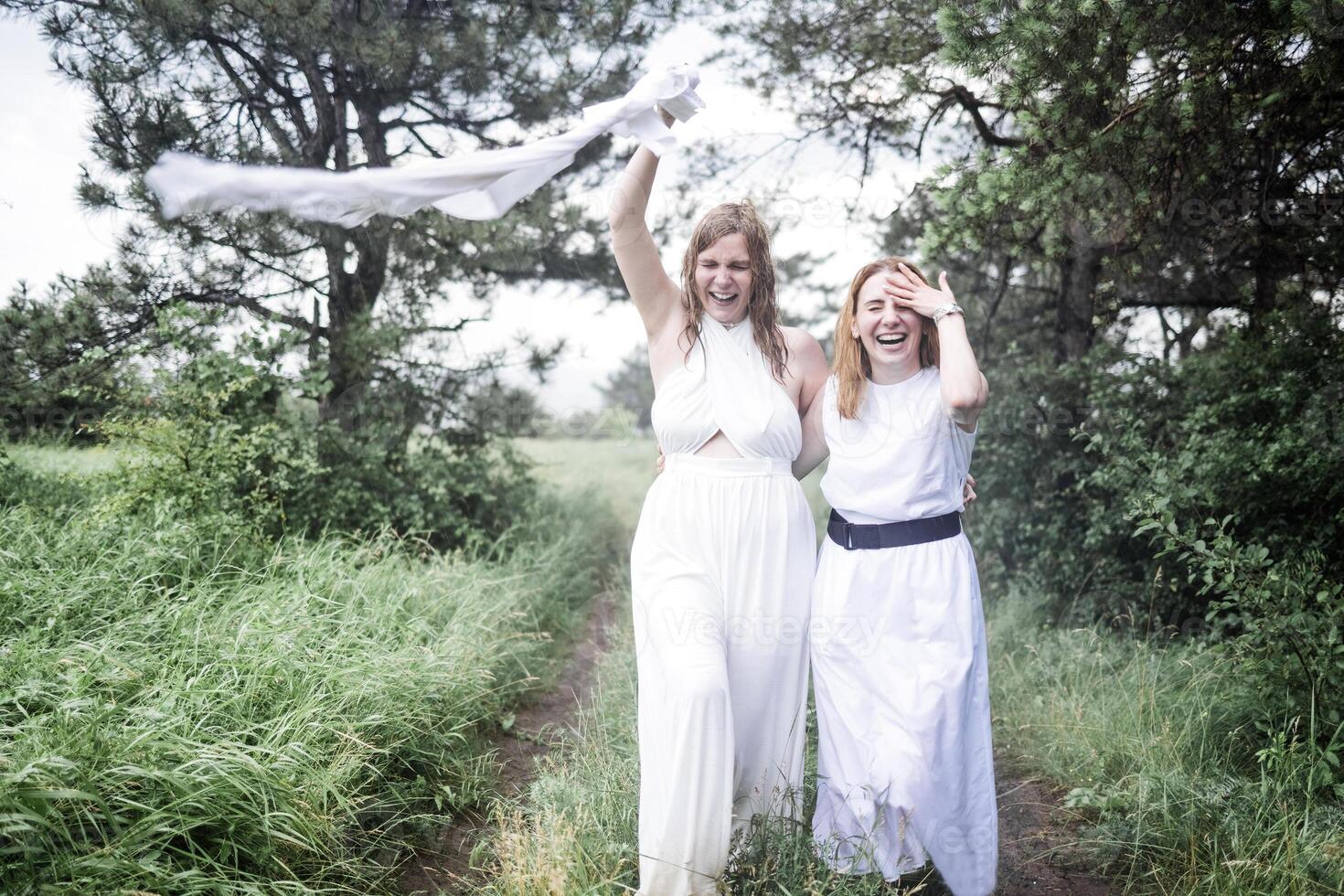 Two charming girls in white dresses are running in the summer rain photo