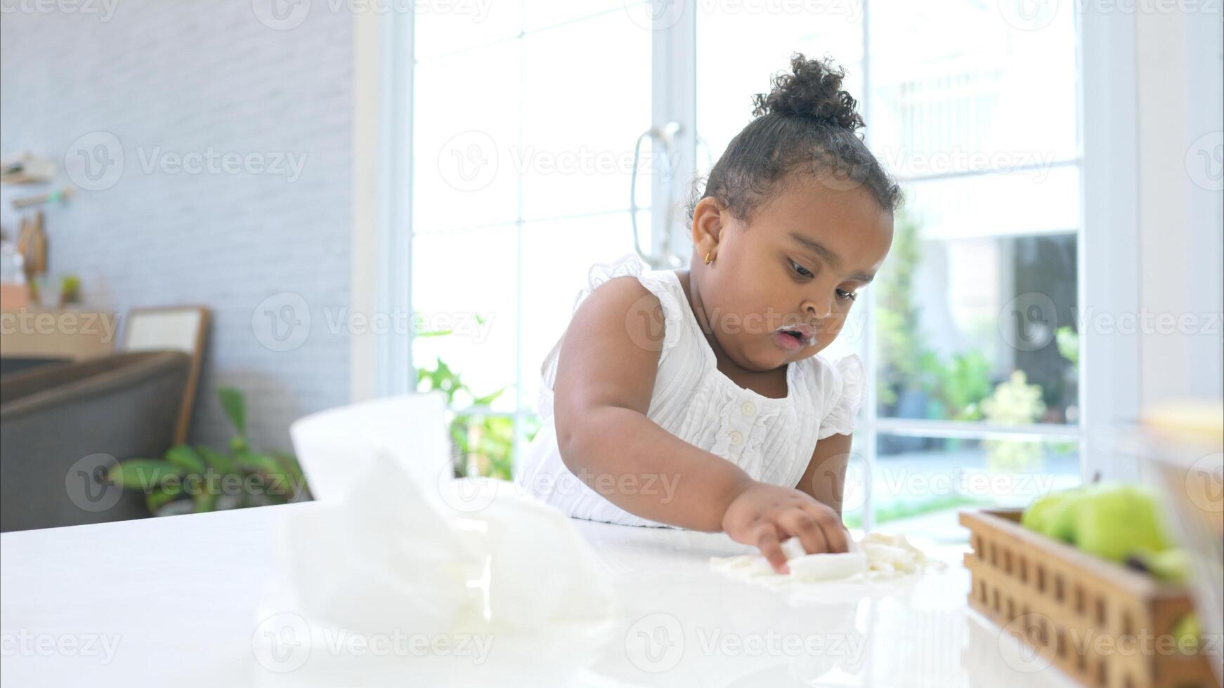 A tiny girl clean the table and floor after glass of milk spilled while drinking photo