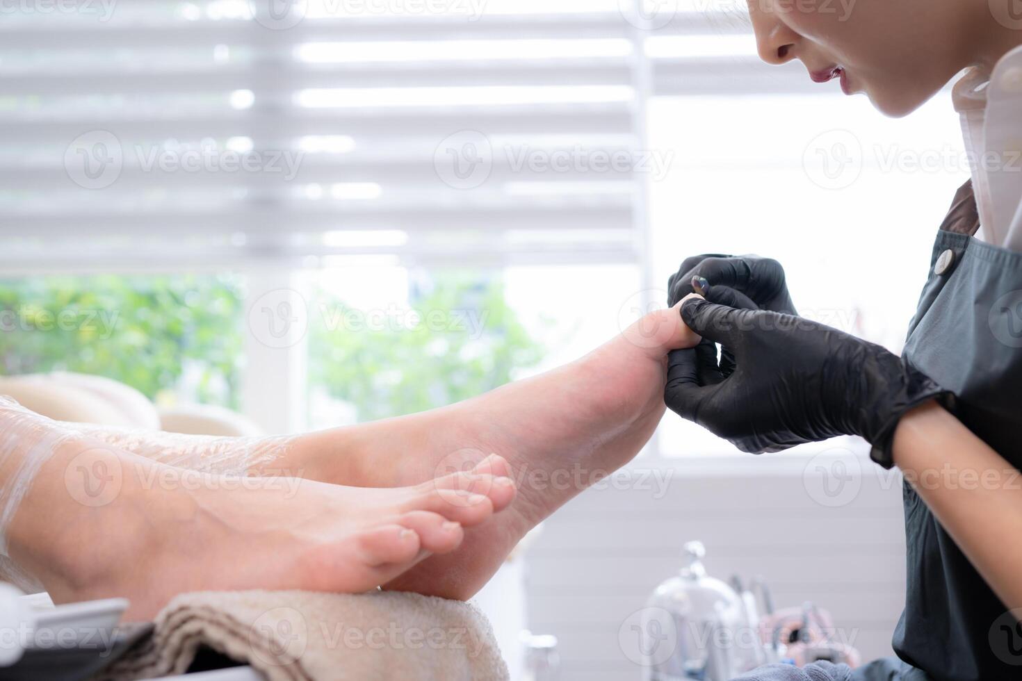 A nail technician is using tools to cut and polish foot of a customer. photo
