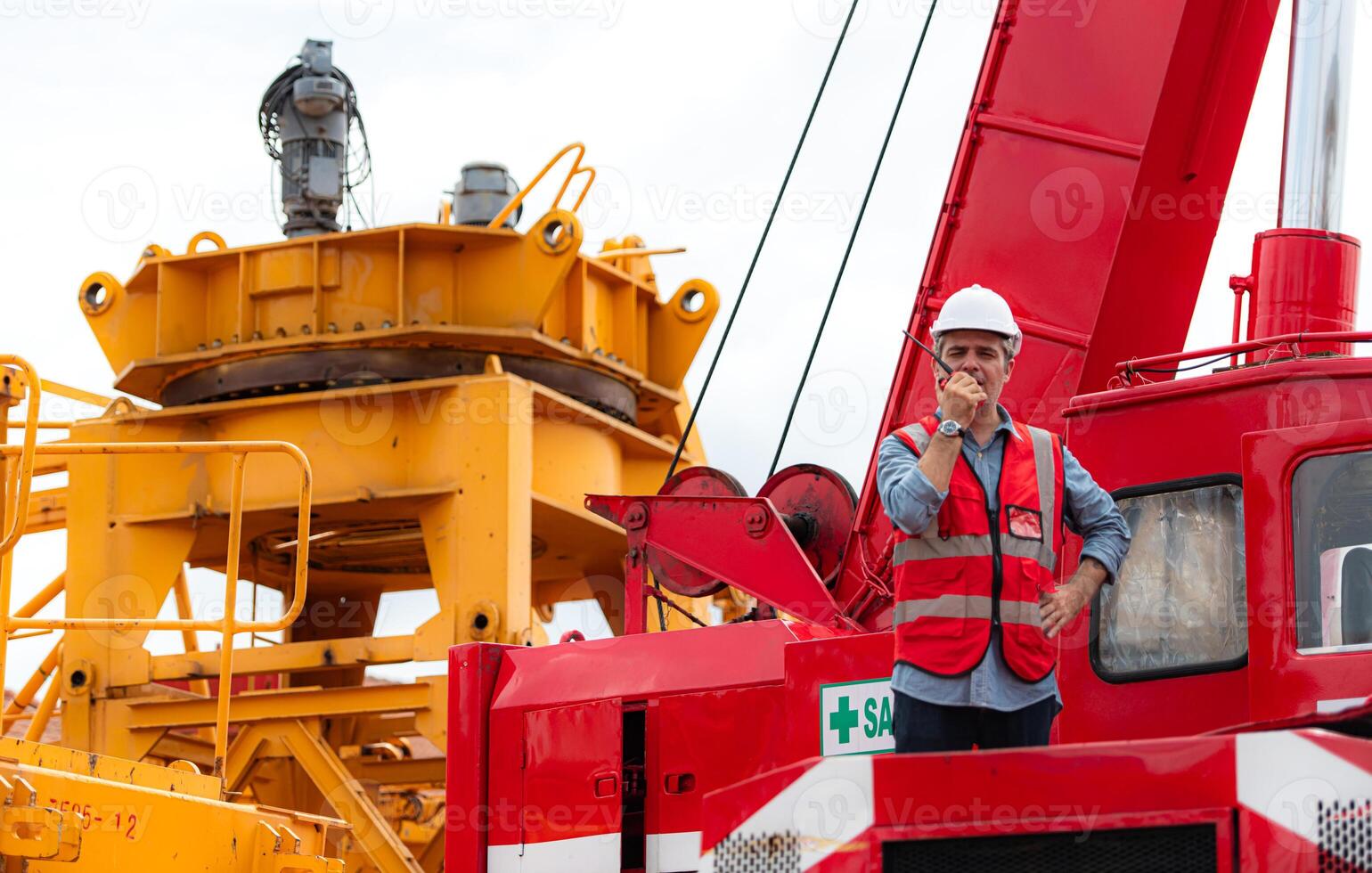 Crane foreman uses walkie-talkie and inspect the construction crane lifting heavy items in the storage warehouse for assembly on the construction site photo