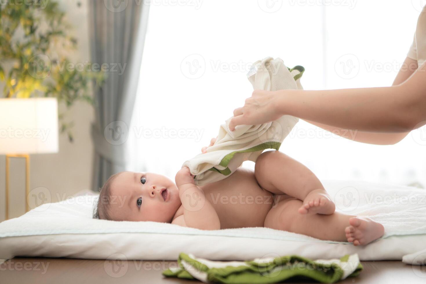 A tiny child smiles happily on the bed waiting for mother apply powder and put on clothes after taking a bath photo