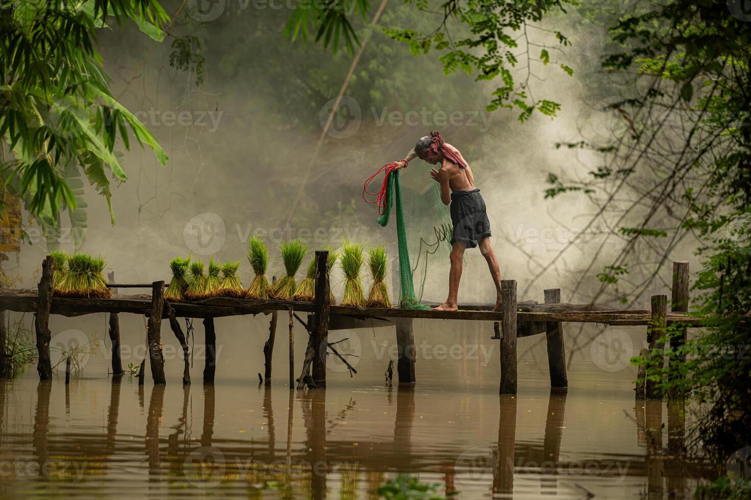 Fisherman atop the bridge netting fish in the river with a fishnet photo