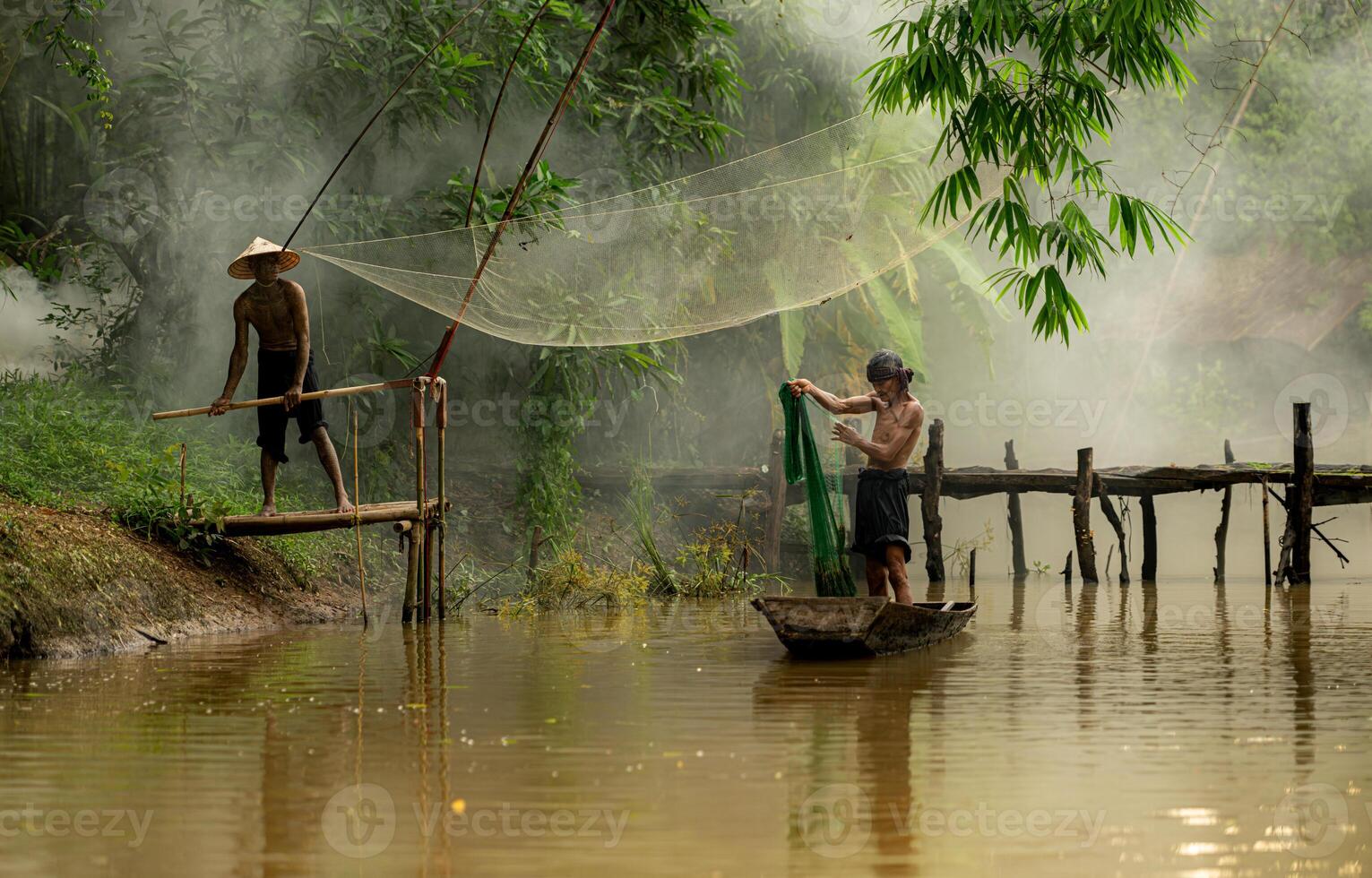 Two farmers on a boat in the river using a fishnet to catch fish photo