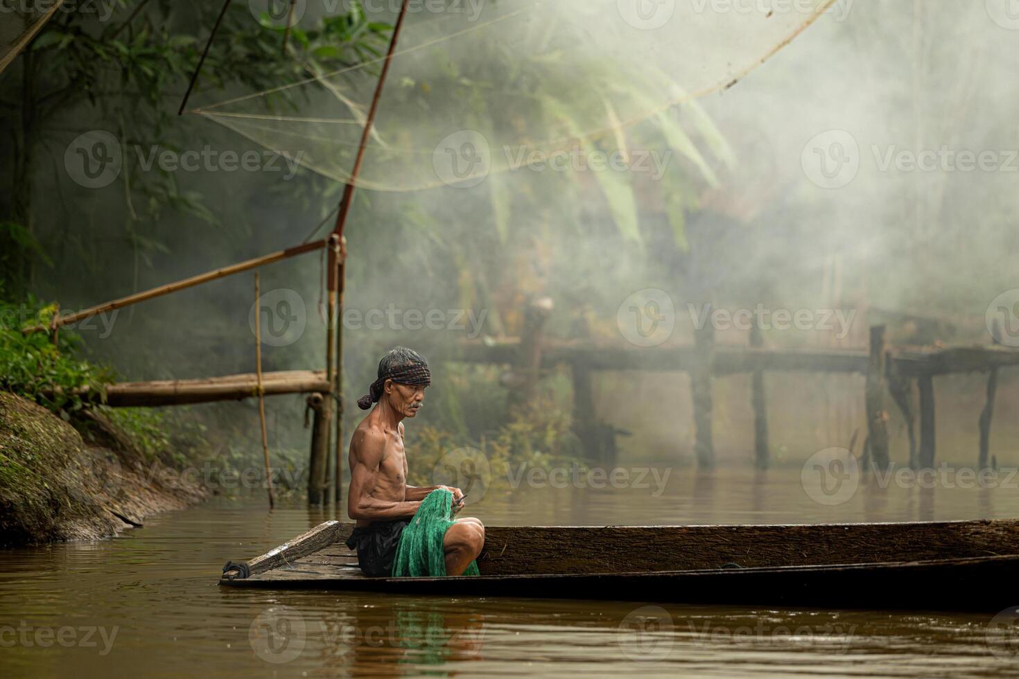 Fisherman on a boat in the river using a fishnet to catch fish photo