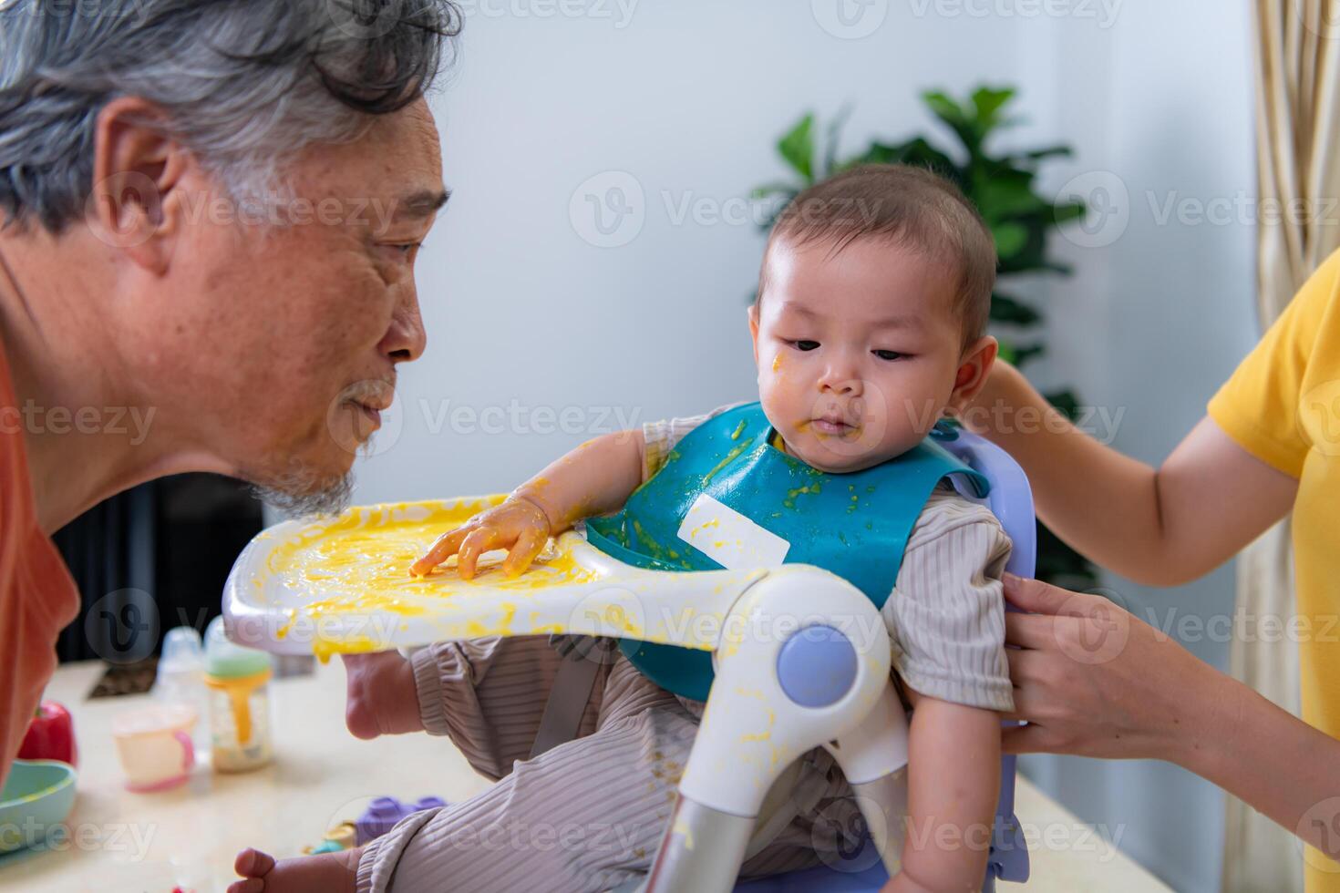 A little child eating his first meal, parents and grandparents cheer excitedly photo