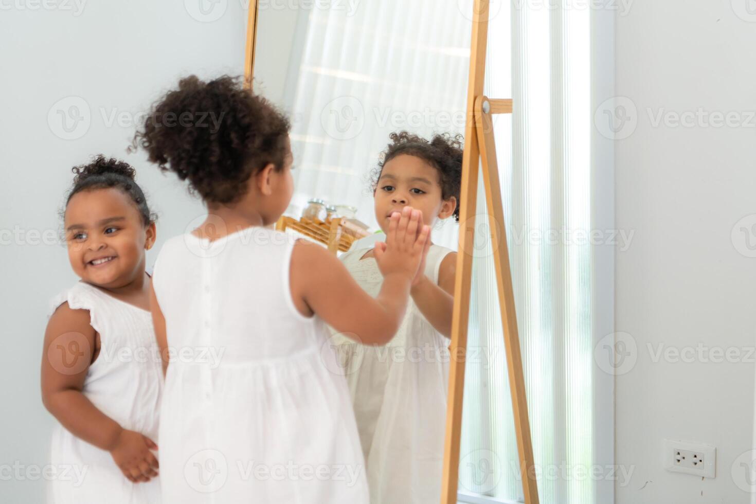 A little girl is looking at herself in the mirror in the dressing room of the house photo