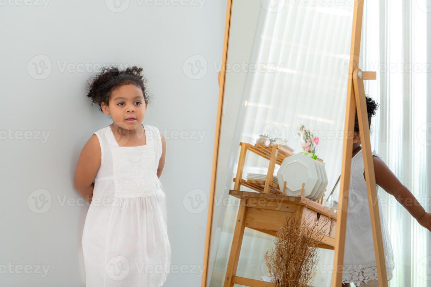 A little girl is looking at herself in the mirror in the dressing room of the house photo