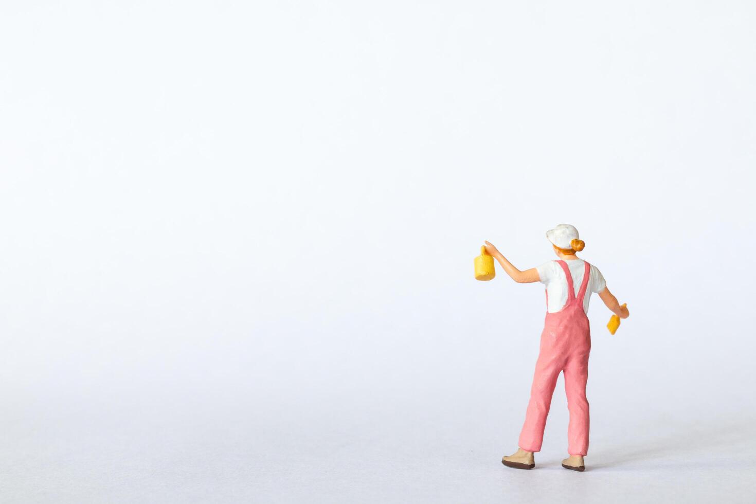 Miniature figure dressed in pink overalls and a white cap on a clean white background photo