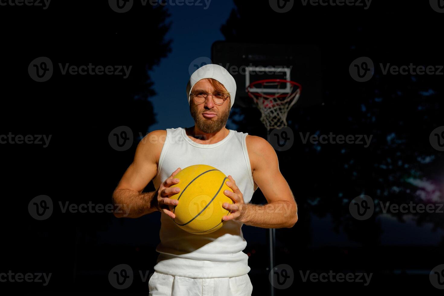 Man holding a basketball in a park at dusk, showcasing athleticism and confidence by the court photo