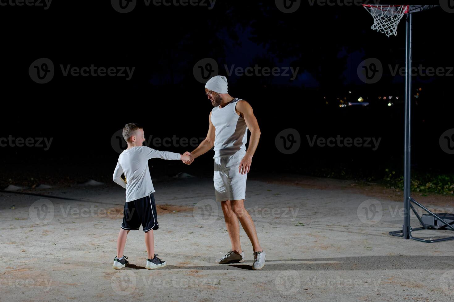 A young man and a boy shake hands before playing basketball in the evening in the park photo