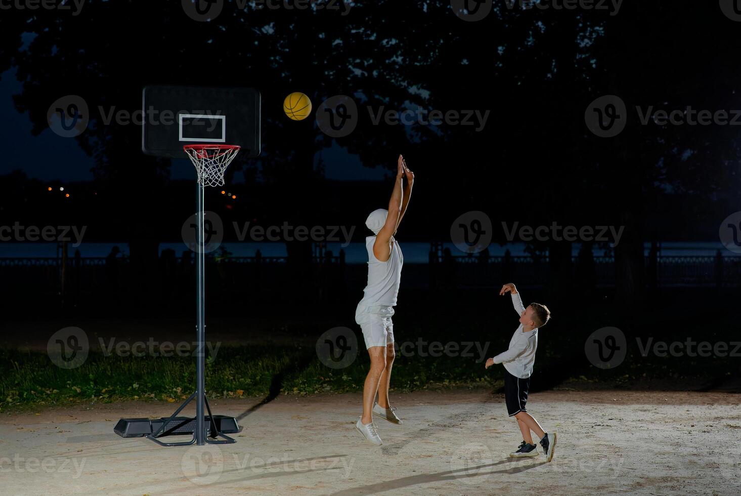 A father and son enjoy a night basketball game at a local park under bright lights focusing on teamwork and fun photo
