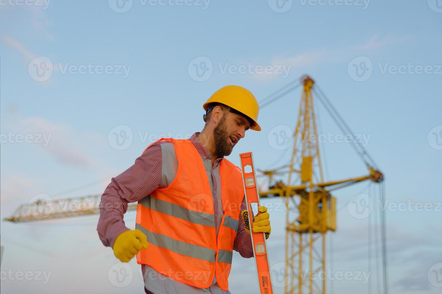 Construction worker wearing safety vest and holding spirit level at construction site photo