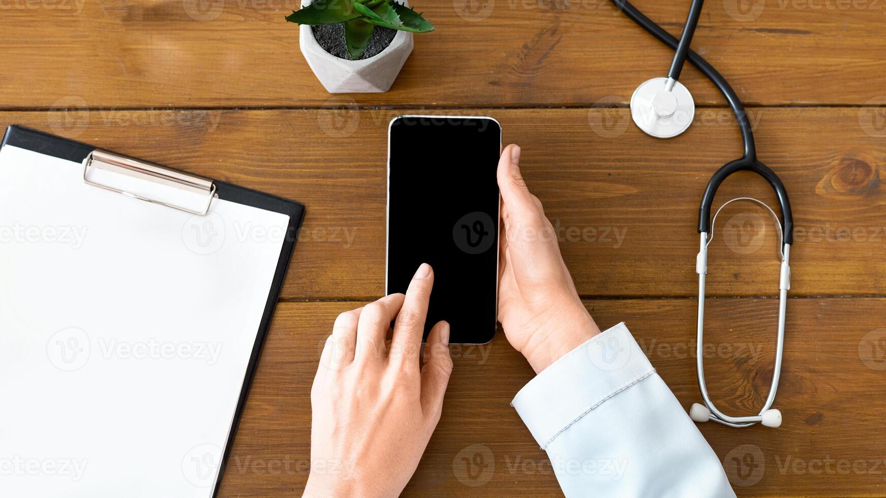 Female doctor is typing on smartphone with blank screen on wooden table with tablet and apple photo
