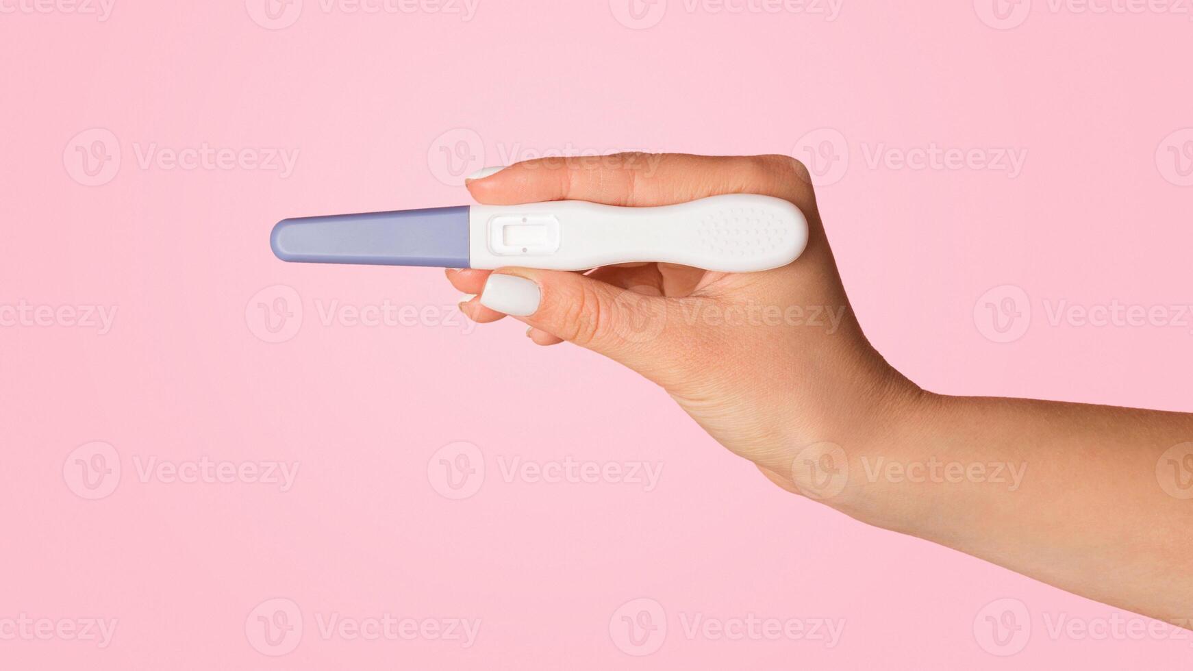 Unrecognizable woman holding blank pregnancy or ovulation test on pink background, closeup view. Copy space photo