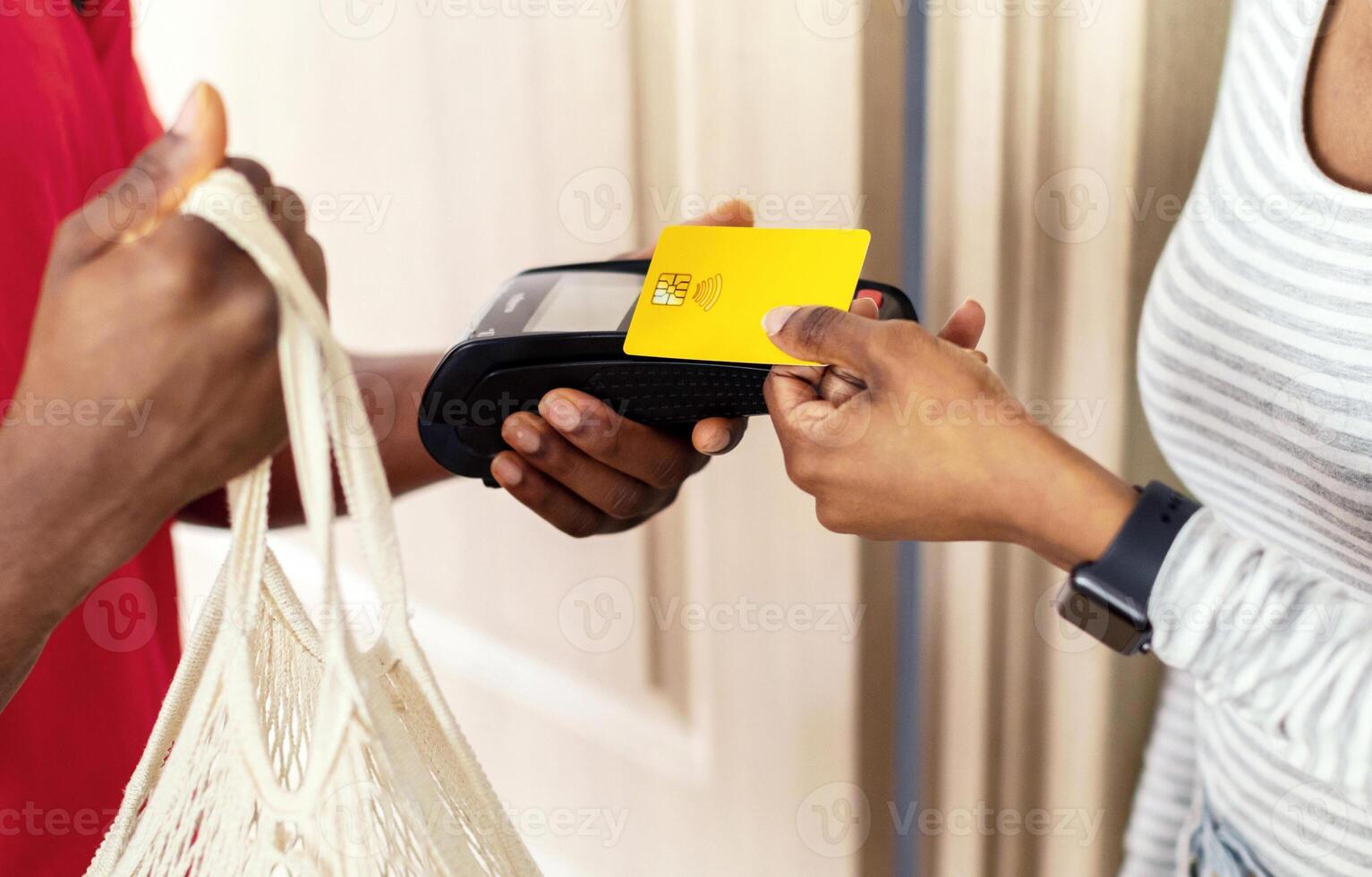 Unrecognizable Black Female Receiving And Paying For Delivered Groceries Putting Credit Card To Payment Terminal Standing With Courier Indoors. Supermarket Food Delivery. Cropped, Selective Focus photo