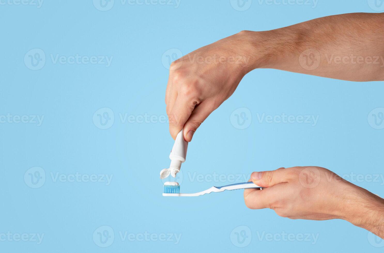 Dental hygiene. Young guy applying paste from tube onto toothbrush against light background, copy space. Panorama photo