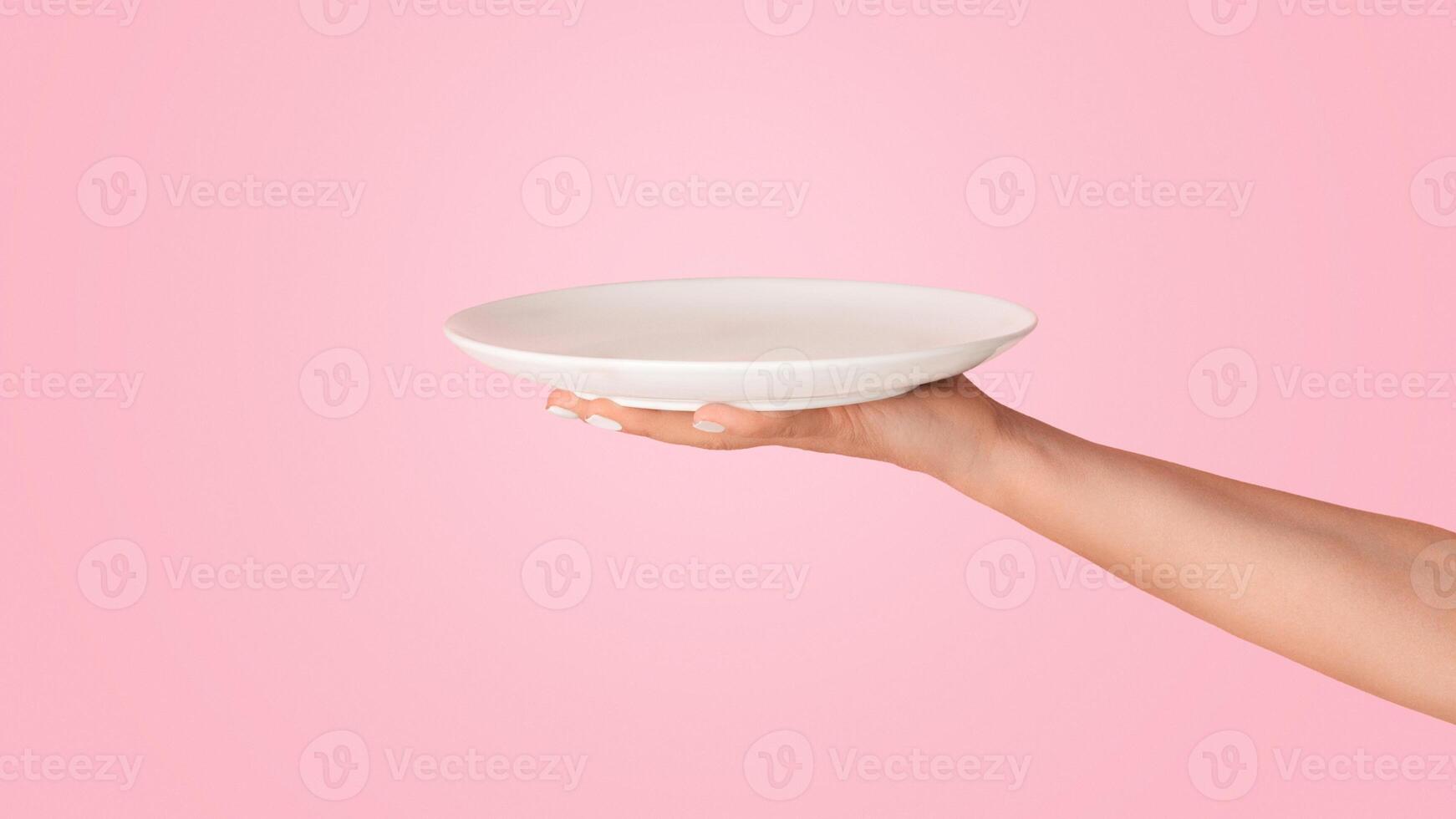 Millennial woman holding empty plate on pink background, mockup for your design photo