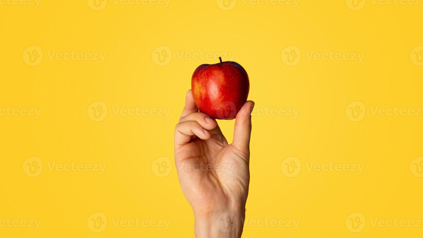 Male hand showing yummy red apple on orange background. Panorama photo