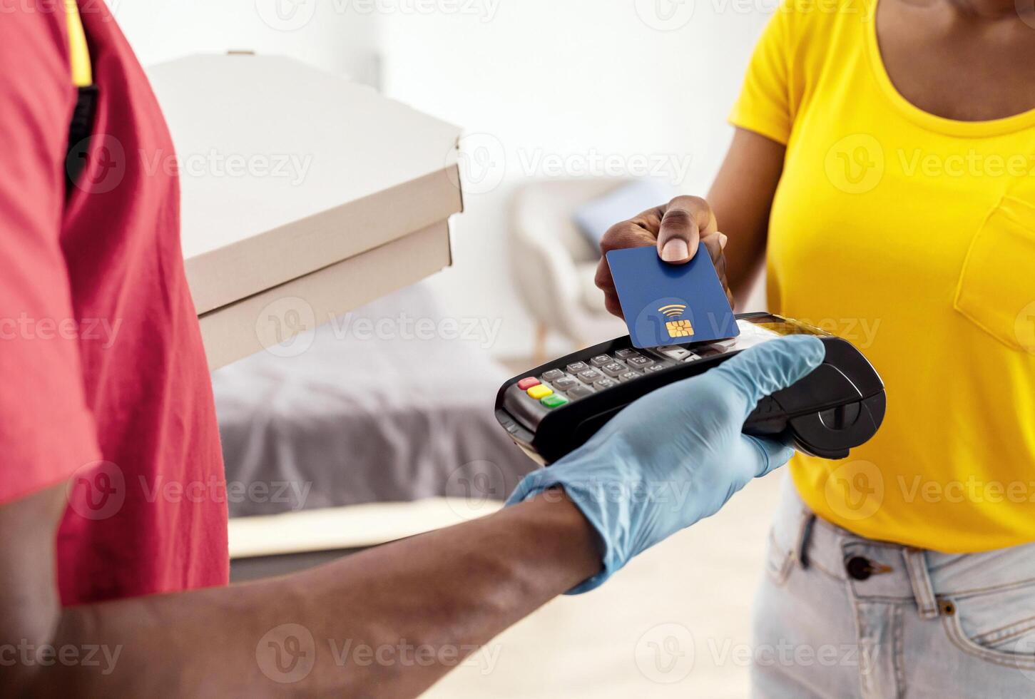 Payment For Pizza Delivery. Unrecognizable Black Female Receiving Food From Courier Paying With Credit Card Standing At Home, Wearing Protective Face Mask. Cropped, Selective Focus photo