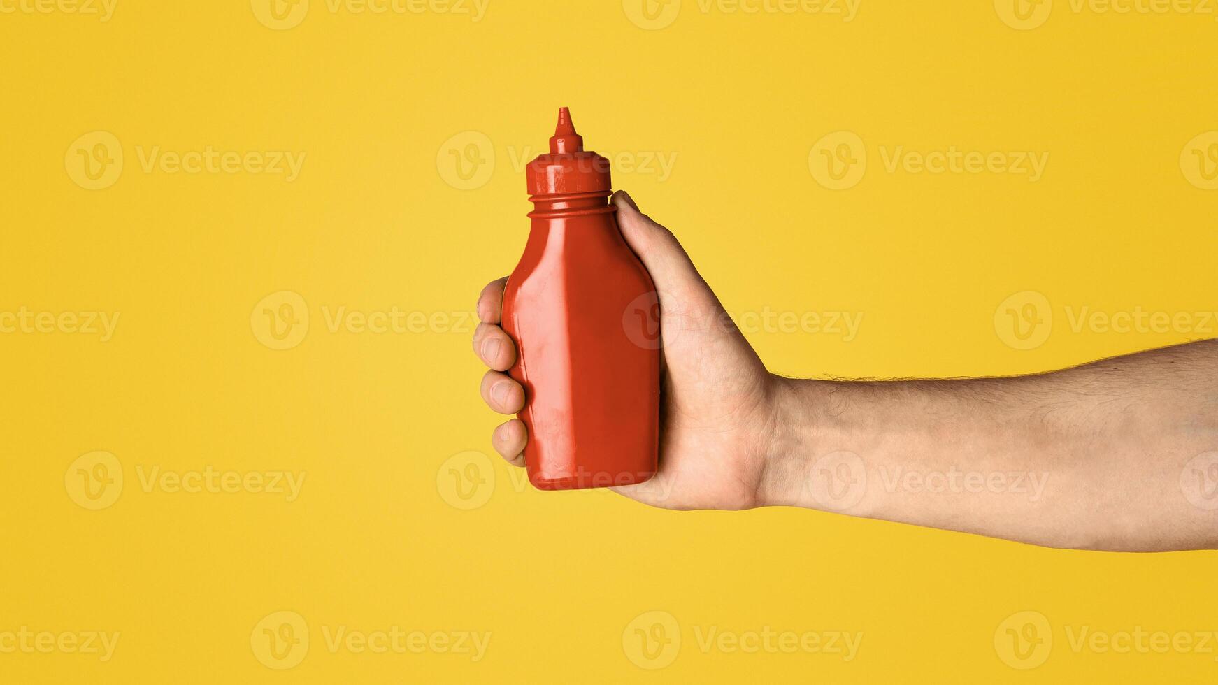 Closeup view of millennial guy showing squeeze bottle of mustard on orange background, mockup for design. Panorama photo