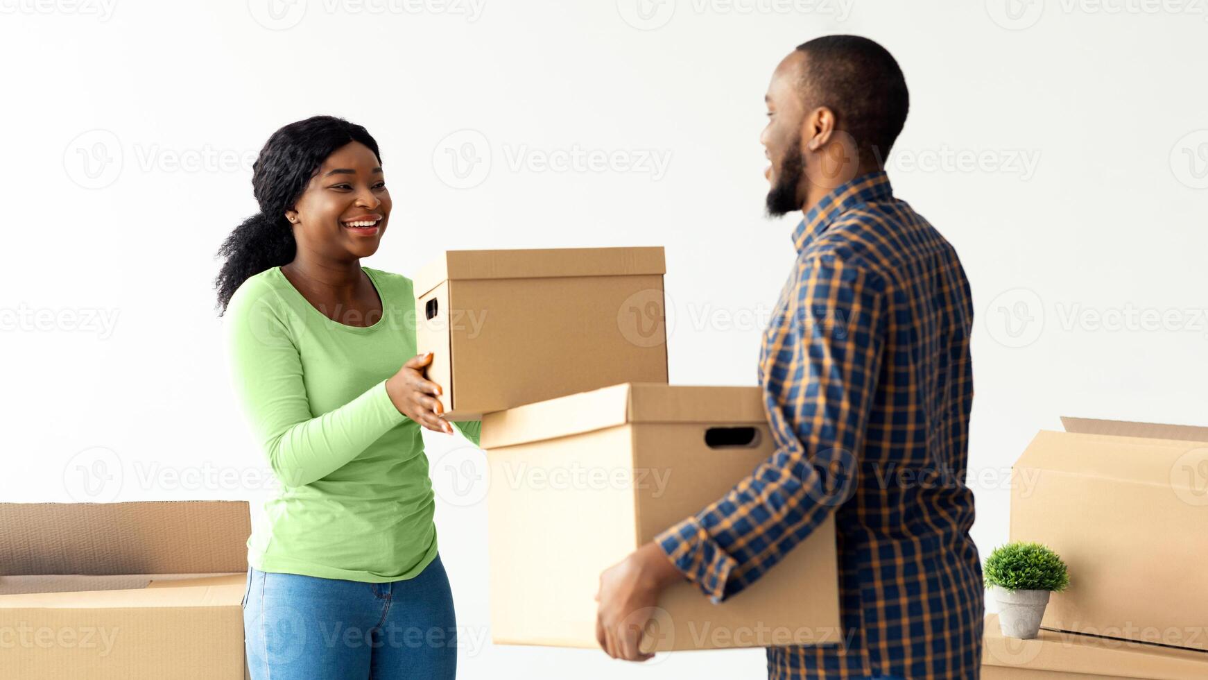 Relocation Day. Portrait Of Happy African American Couple Carrying Cardboard Boxes, Cheerful Black Spouses Moving To New Apartment, Packing Belongings And Smiling To Each Otrher, Free Space photo