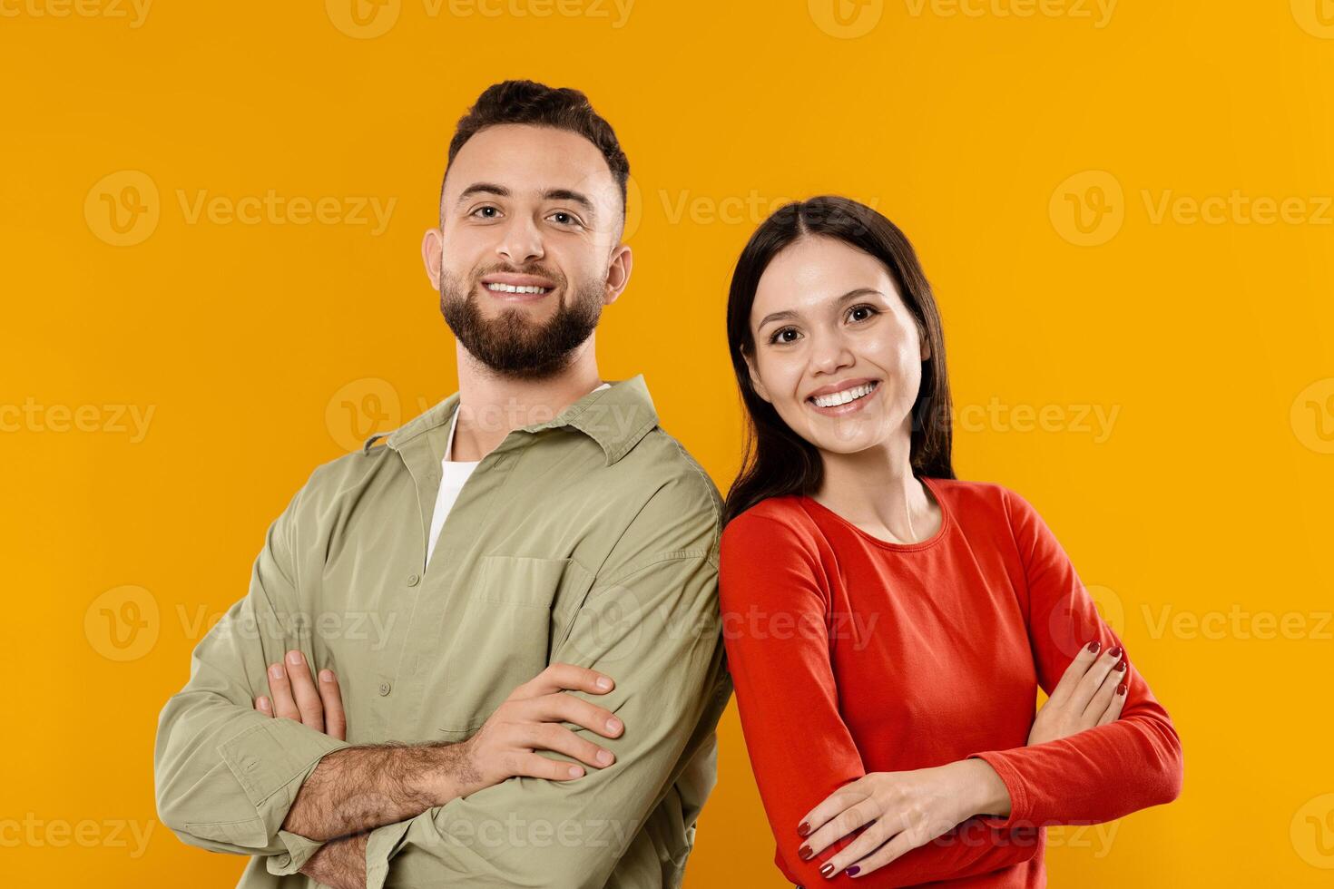 A young couple stands side by side with arms crossed, dressed in complementary outfits. They smile brightly, showcasing their affection and connection in this playful moment. photo
