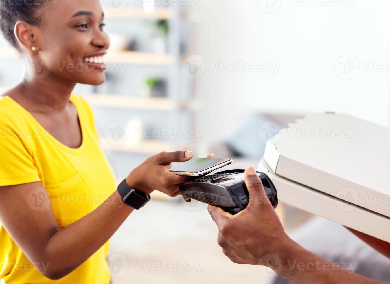 Black Lady Putting Smartphone To Payment Terminal Paying Courier Guy For Pizza Using Cellphone Standing At Doorway Of Her Home. Mobile Banking, Food Delivery Service. Selective Focus photo
