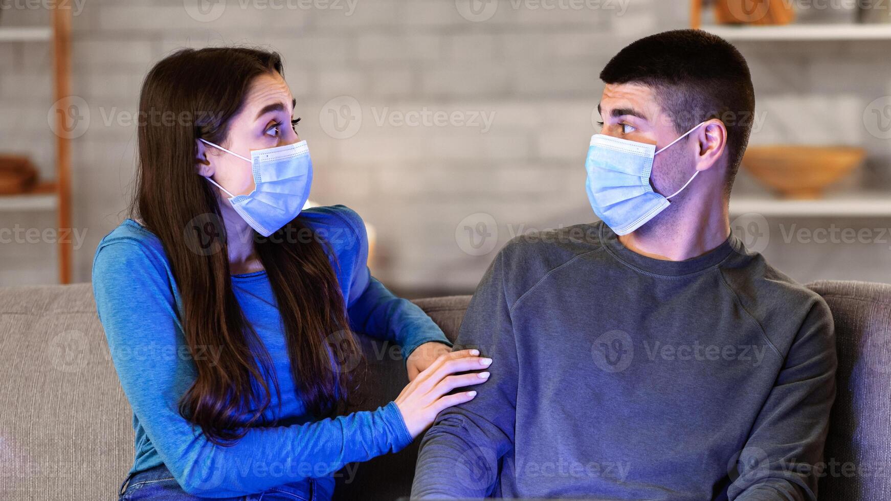 Coronavirus Panic. Scared couple in surgical masks emotionally reacting to disease outbreak news, using laptop sitting on sofa photo