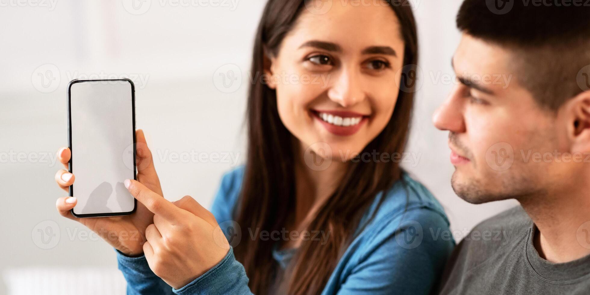 New Mobile App. Cheerful girl holding and pointing at smartphone with black screen for mockup, copy space photo