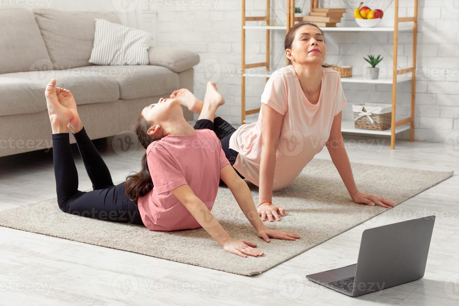 Covid lockdown sports. Teen girl and her mother doing yoga flexibility poses to tutorial course at home. Kid and parent engaged in domestic fitness, exercising with online trainer indoors photo