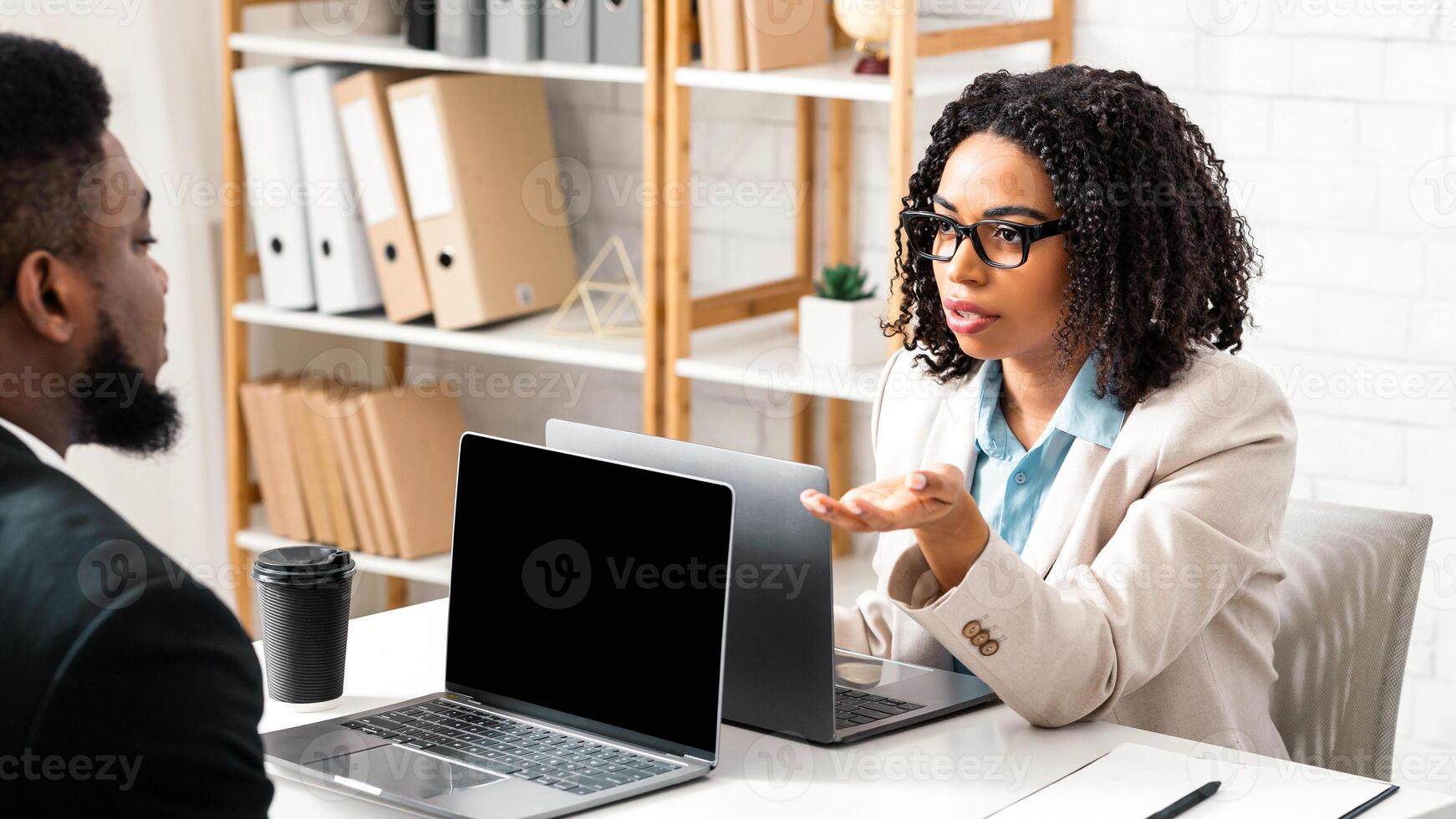 Serious black woman speaking to her male colleague at company office, asking about common project, copy space. Teamwork and cooperation at workplace concept photo