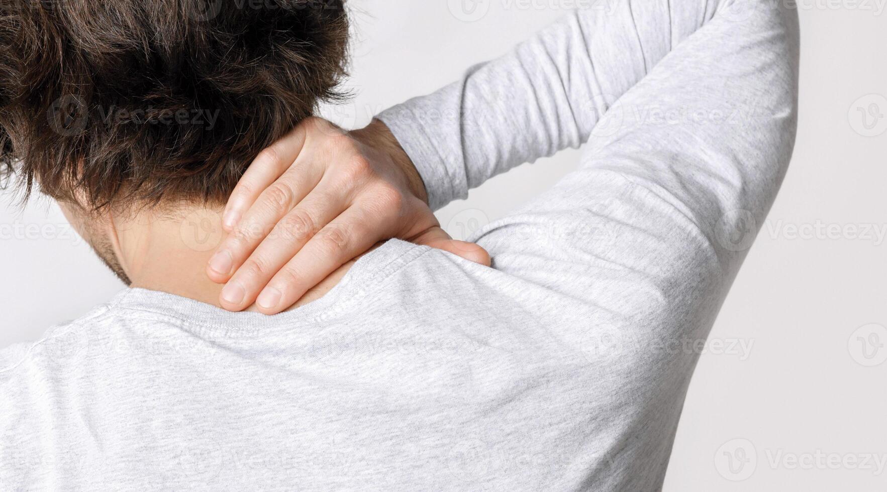 Pain in neck from work. Guy presses his hand to sore spot, back, close up, studio shot photo