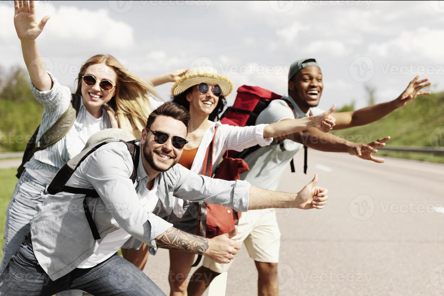 Cheerful young people standing on roadside, stopping car, trying to get free ride, having autostop journey, free space. Exciting travel adventure, hitchhiking with friends, summer holidays concept photo