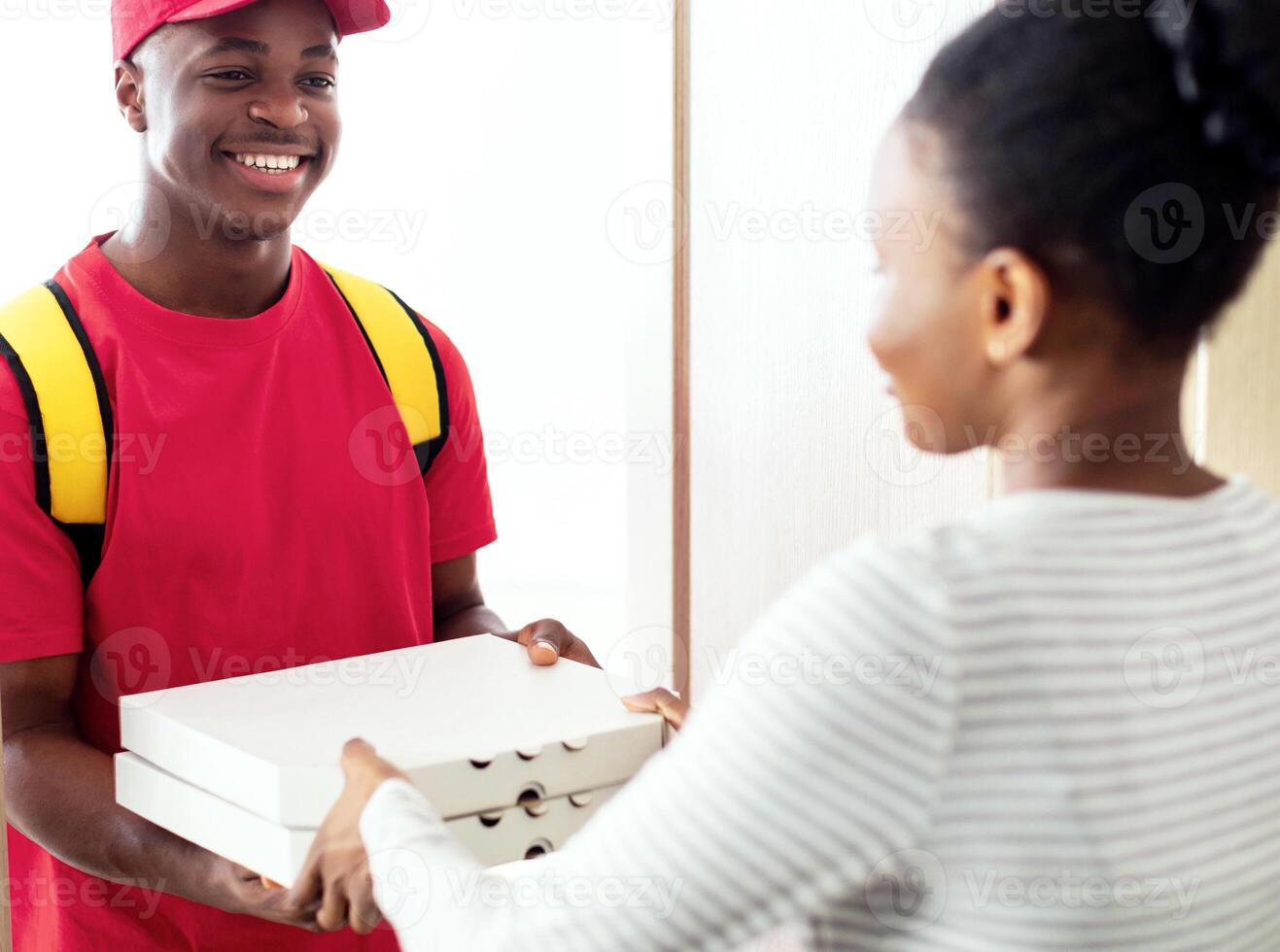 Food Delivery. Cheerful Black Male Courier Standing Holding Pizza Boxes Smiling To Customer Lady In Doors Of Her Home, Selective Focus. Cafe And Restaurant Delivery Service photo