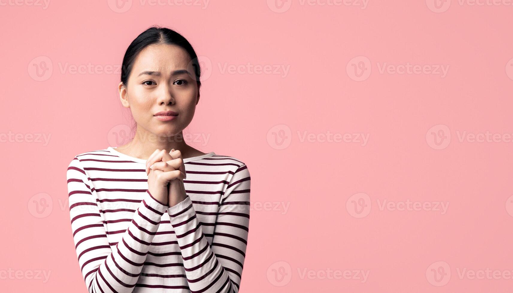 Please. Young asian female begging for something with clasped hands and looking at camera, desperate sad korean woman pleading and asking for help while standing over pink background, copy space photo