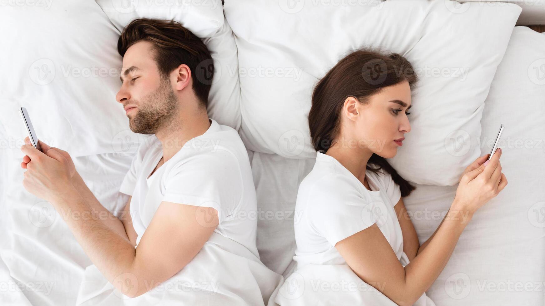 Marital Crisis, Indifference. Couple Using Cellphones Lying Back-To-Back In Bed Indifferent To Each Other. Millennial Spouses Ignoring One Another Texting With Lovers At Home. View From Above photo