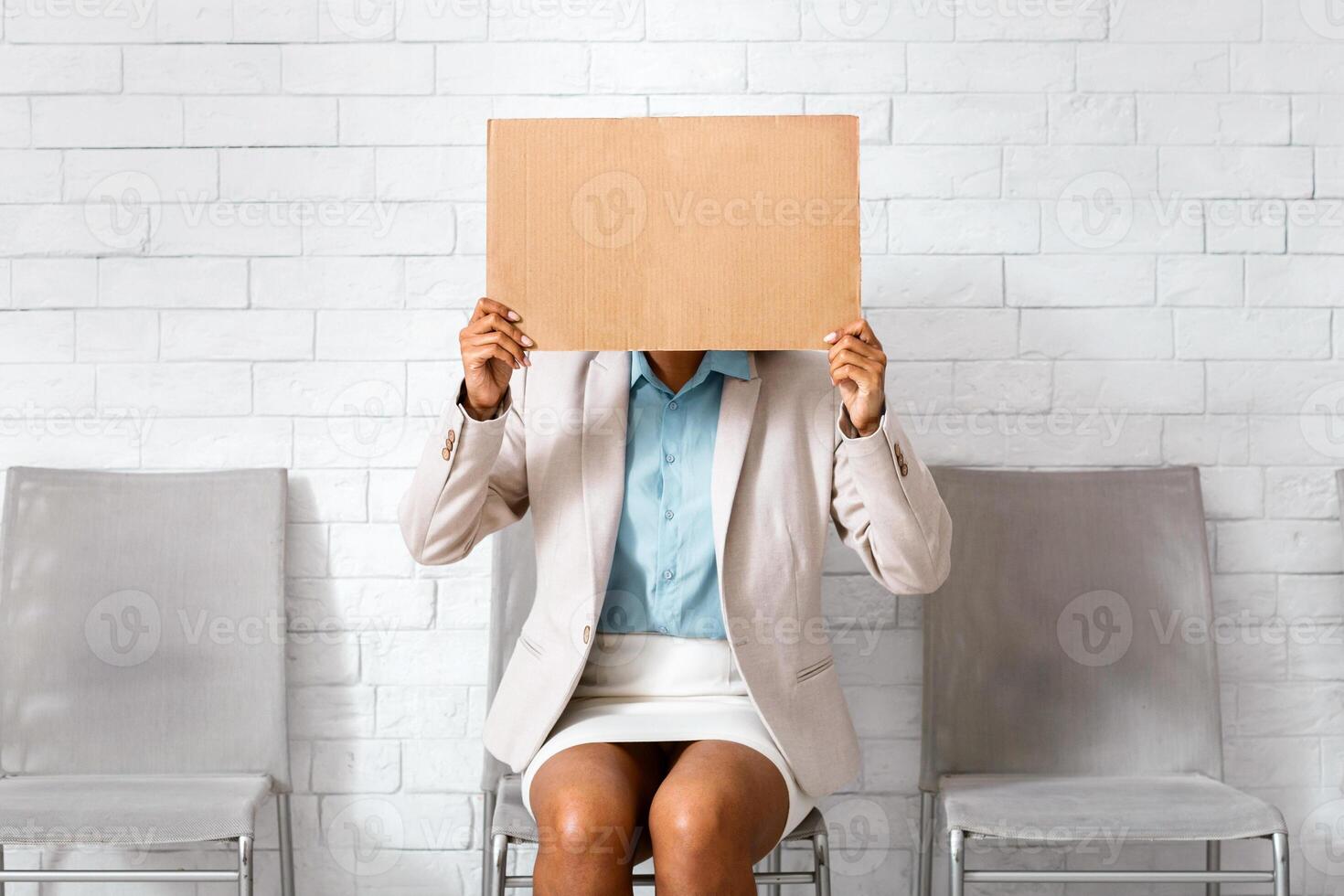 African American woman in business wear hiding behind sign with inscription I NEED WORK while waiting for work interview at office photo