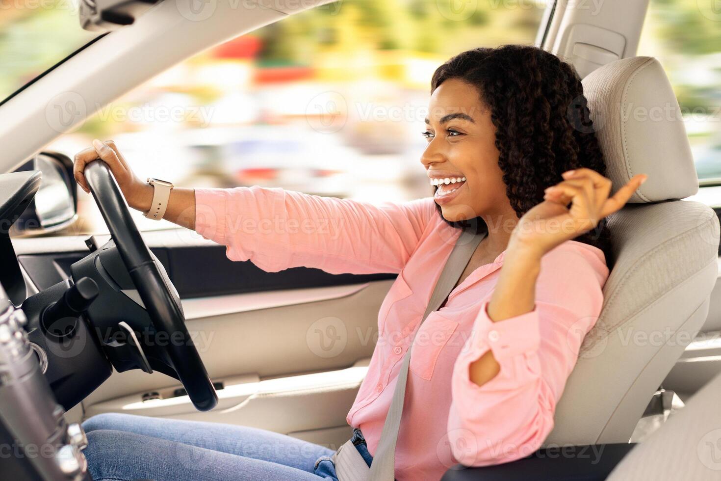 Road Trip Concept. Profile side view portrait of excited playful black woman driving luxury car, dancing to music and singing favorite song, resting on weekend going on vacation or home from work photo