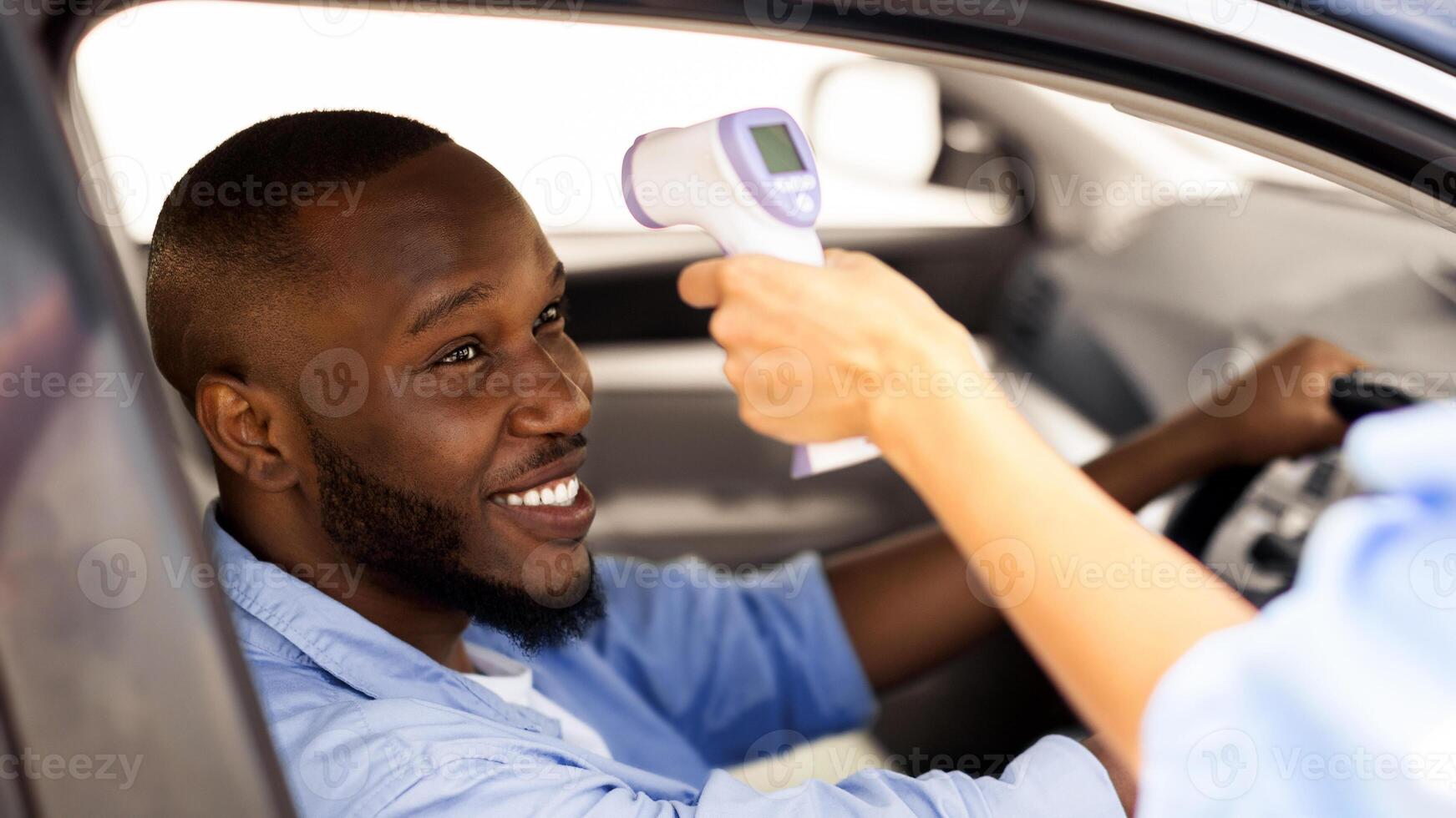 Medical worker or security staff measuring body temperature of young male driver with thermometer outdoors. Lady checking disease symptoms through open window using infrared gun. Prevention And Safety photo