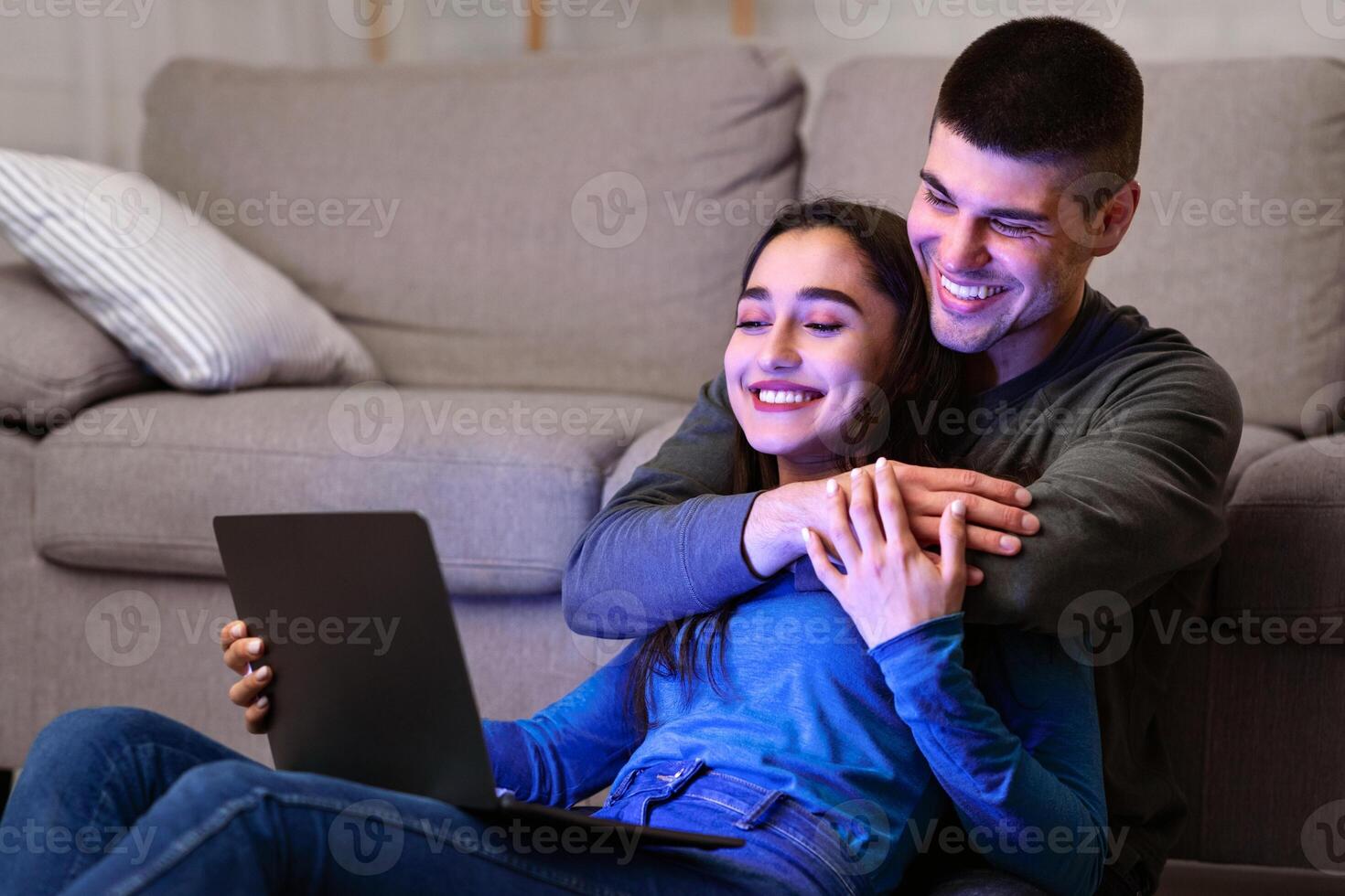 Leisure Concept. Cheerful Young Spouses Using Computer Watching Film Relaxing On Floor Indoor photo