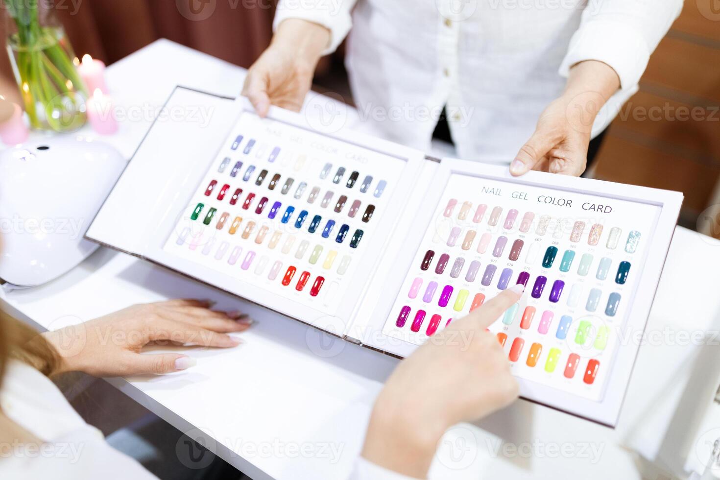 Two women enjoy a pampering experience in a salon. One points at a color chart while choosing nail polish shades, highlighting hands and fashion creativity. photo