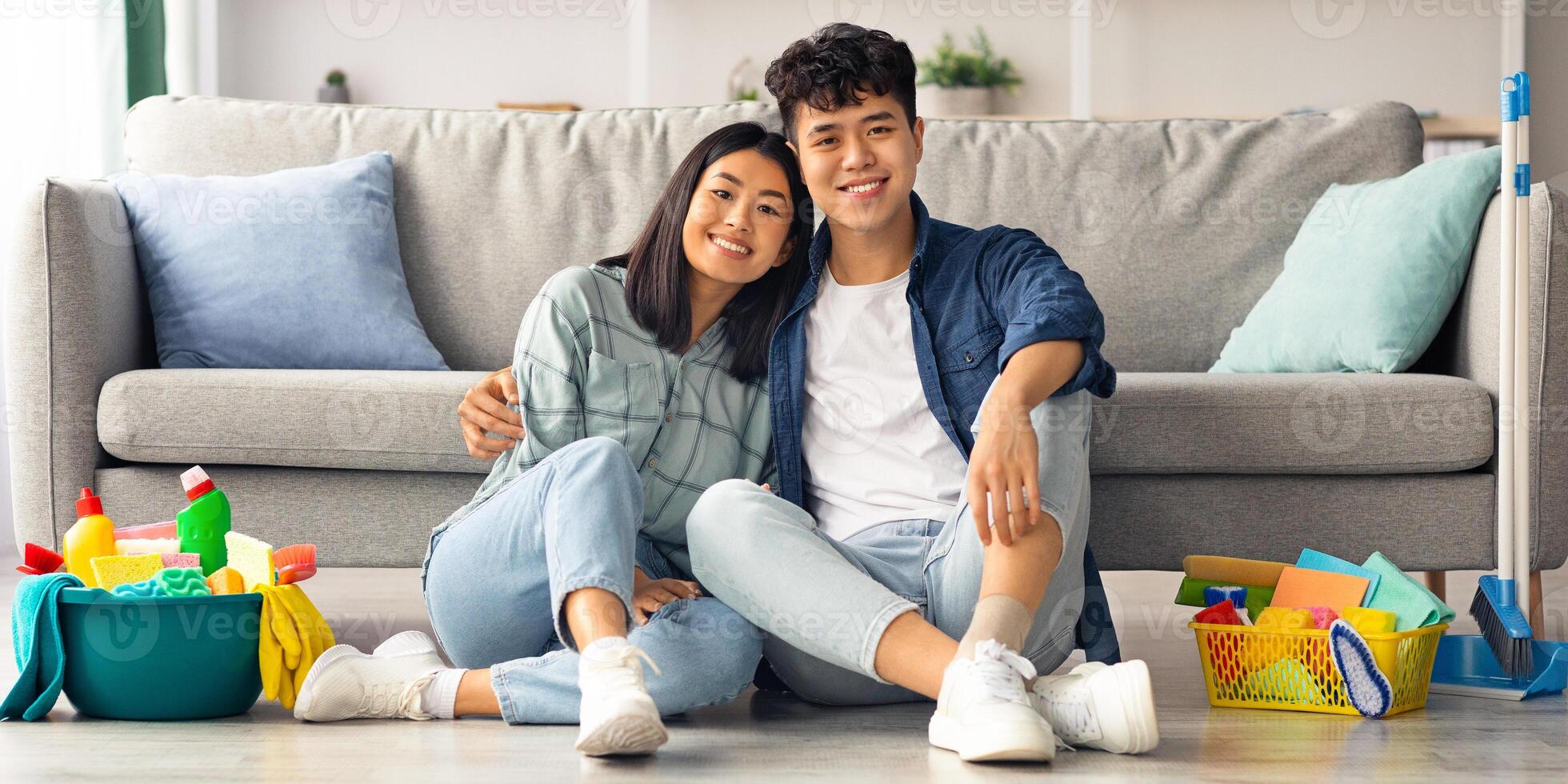 Happy asian couple sitting on floor at home, resting after house-keeping, embracing. Loving young man and woman having break while cleaning their new cozy apartment, panorama with copy space photo