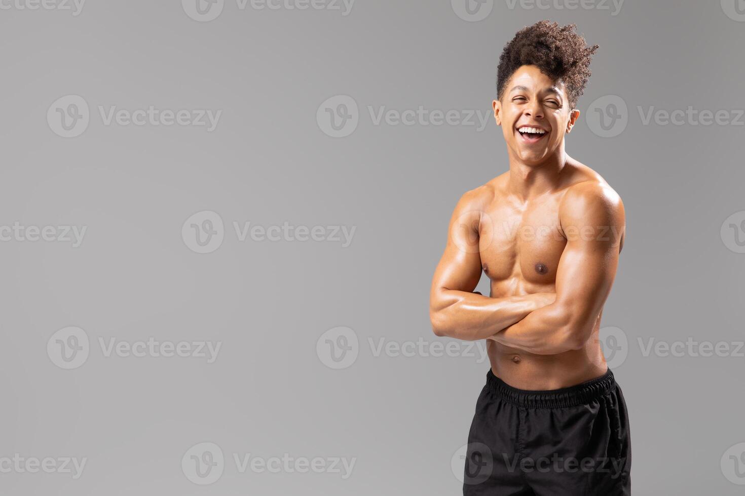 A young Brazilian man stands confidently in a studio, displaying his athletic physique with a big smile. He embraces a healthy lifestyle, exuding energy and positivity, copy space photo