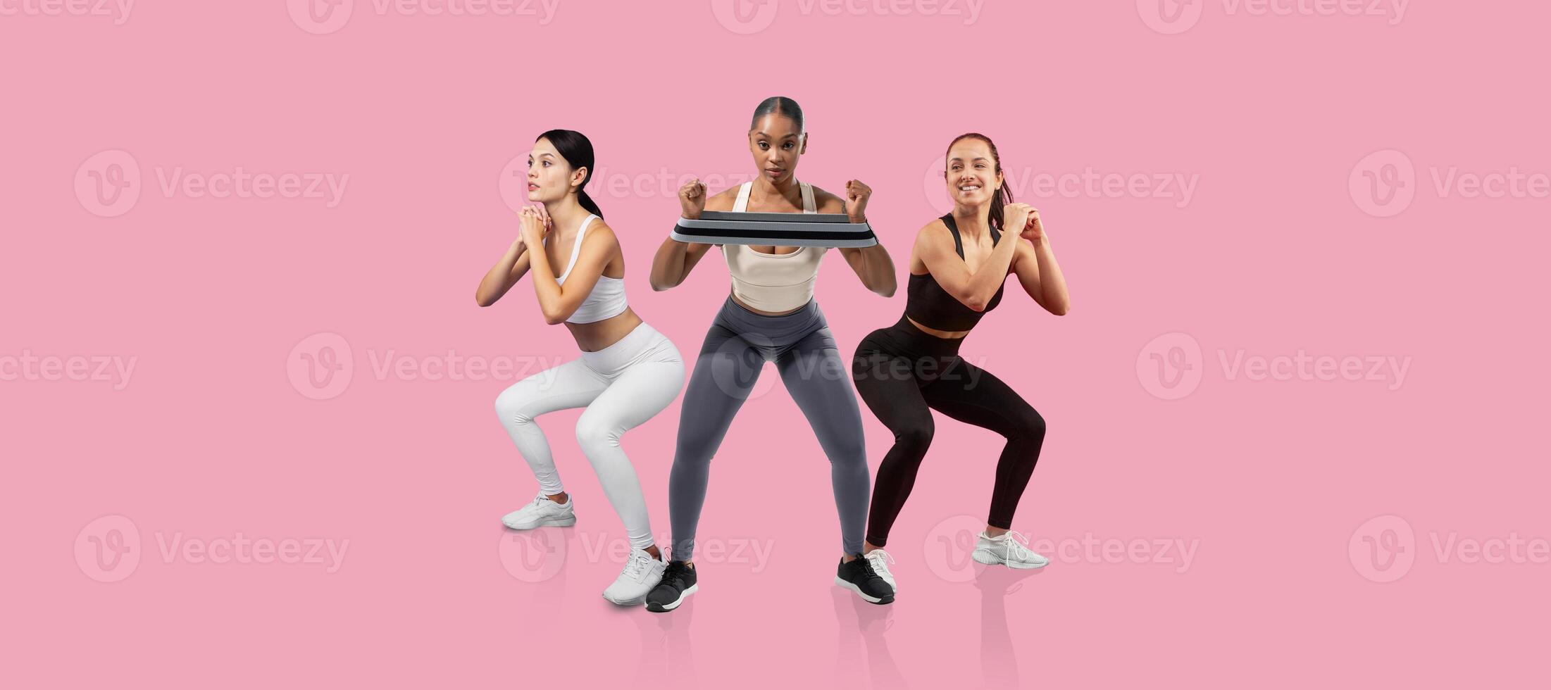 Three women engage in a squat exercise, showcasing their fitness routines in stylish workout attire. The bright pink background adds a vibrant touch to their focused activity. photo