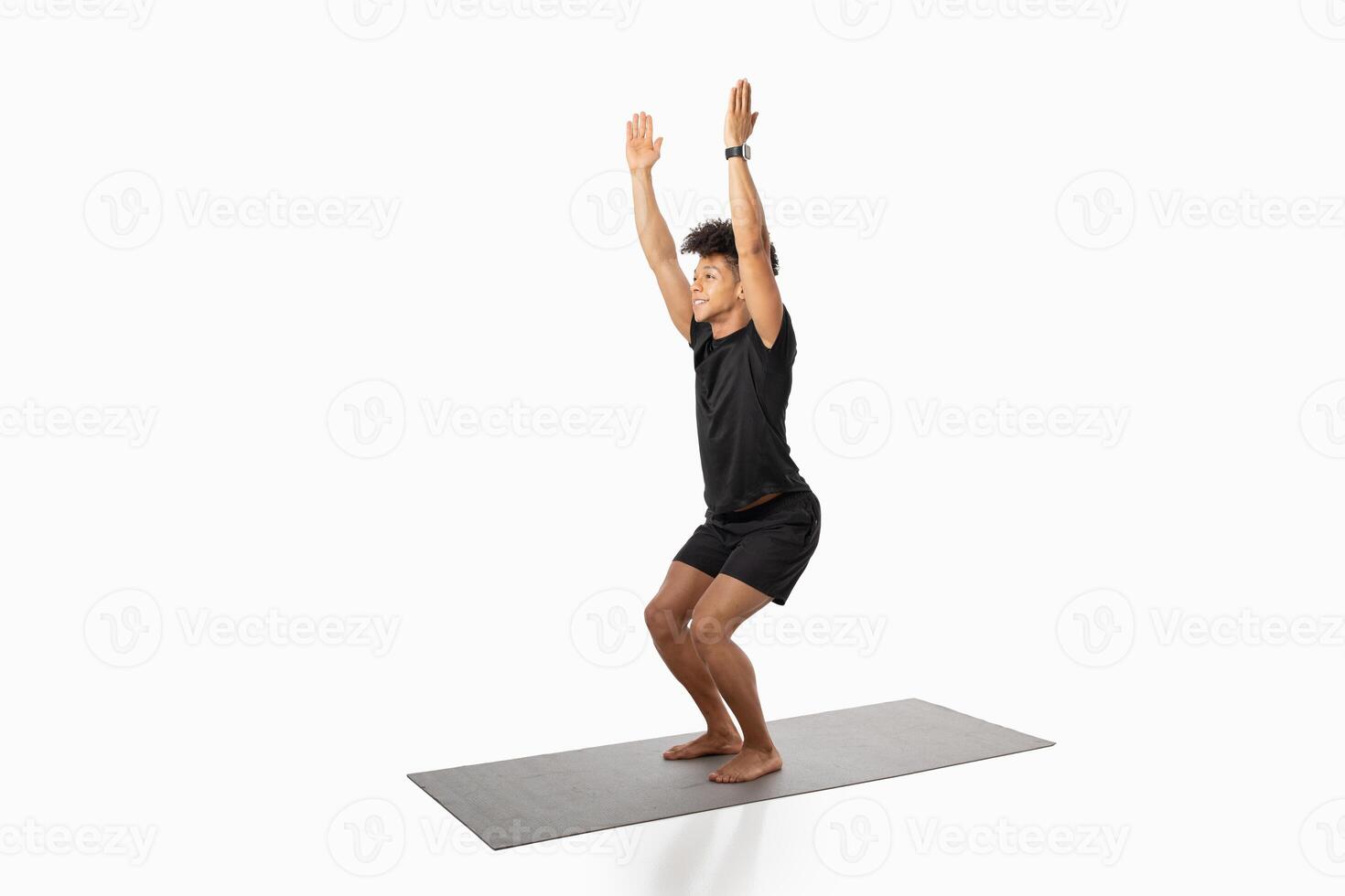 A young Brazilian man is engaged in a fitness workout at home, practicing a squat with arms raised to promote strength and endurance. He exemplifies a commitment to a healthy lifestyle. photo