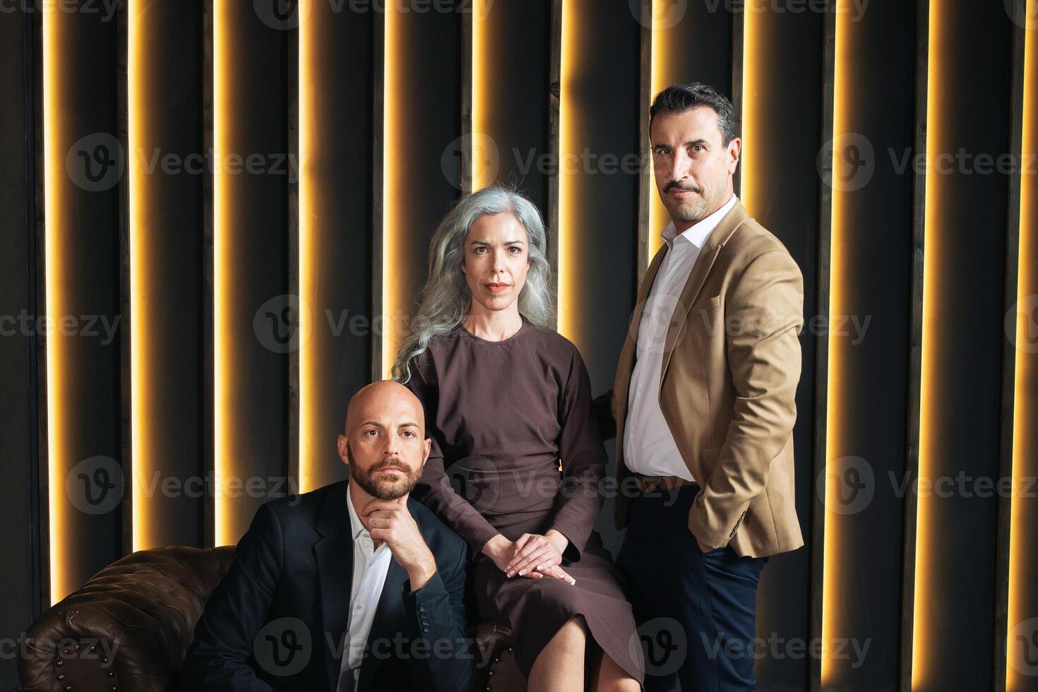 Three professionals, including woman and two men, stand confidently in a contemporary office. The warm lighting and modern decor create an inviting atmosphere for collaboration. photo