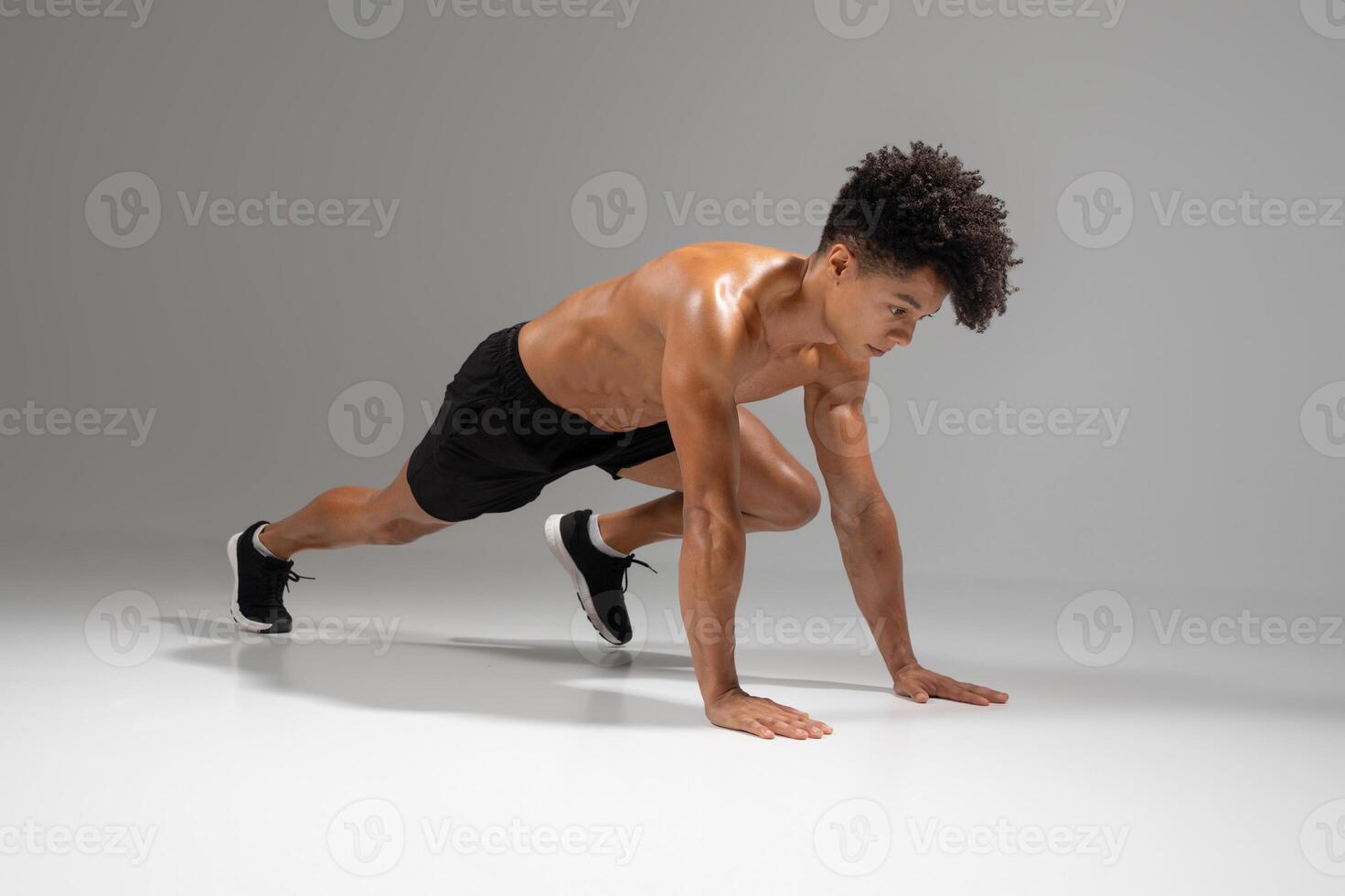 A young Brazilian man is engaged in a mountain climber workout on a smooth surface. He showcases his athletic build and fitness skills, demonstrating a healthy lifestyle indoors. photo