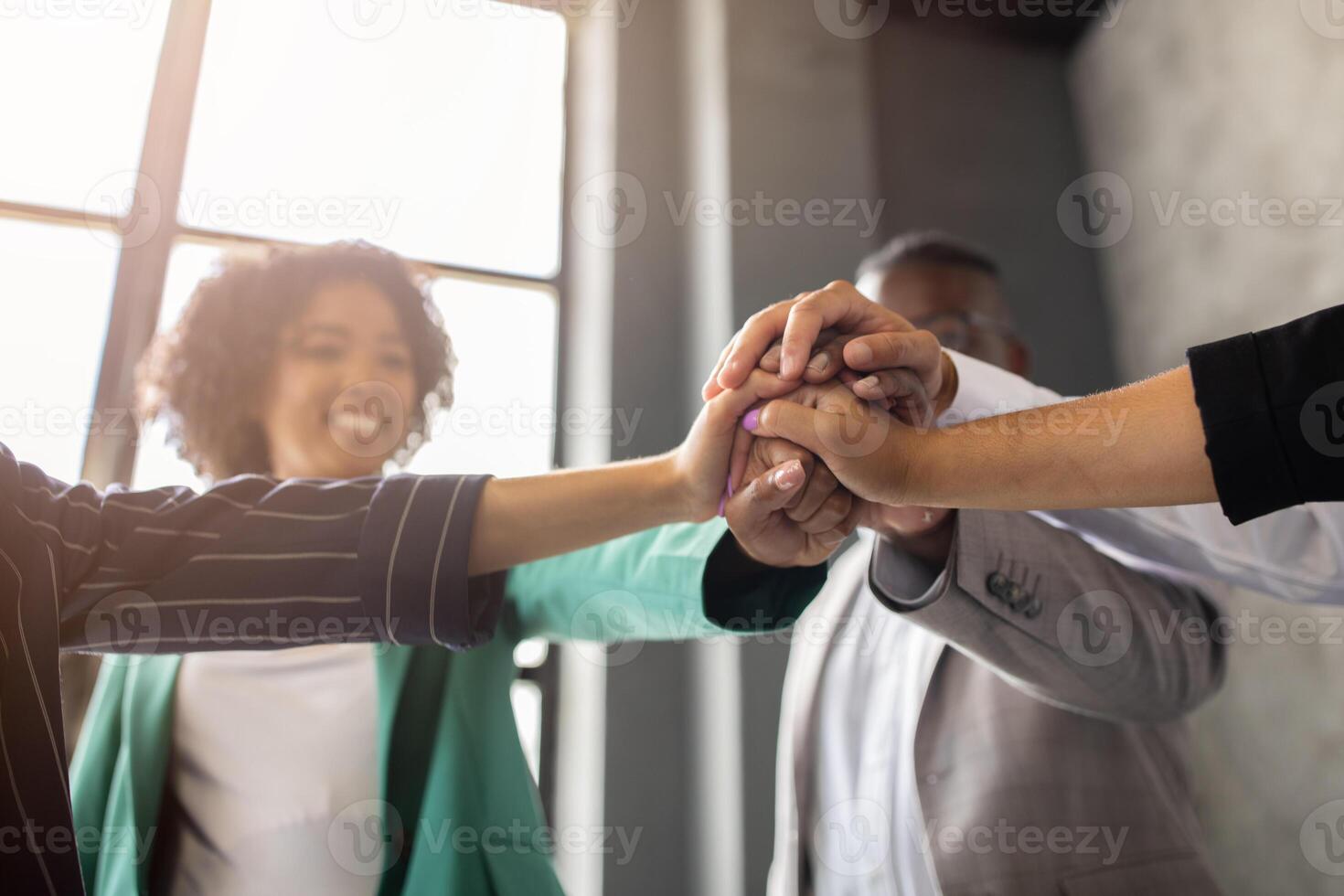 A diverse group of professionals at a corporate office collaborates enthusiastically, showcasing teamwork and unity. Their hands join in a celebratory gesture, highlighting a successful meeting. photo